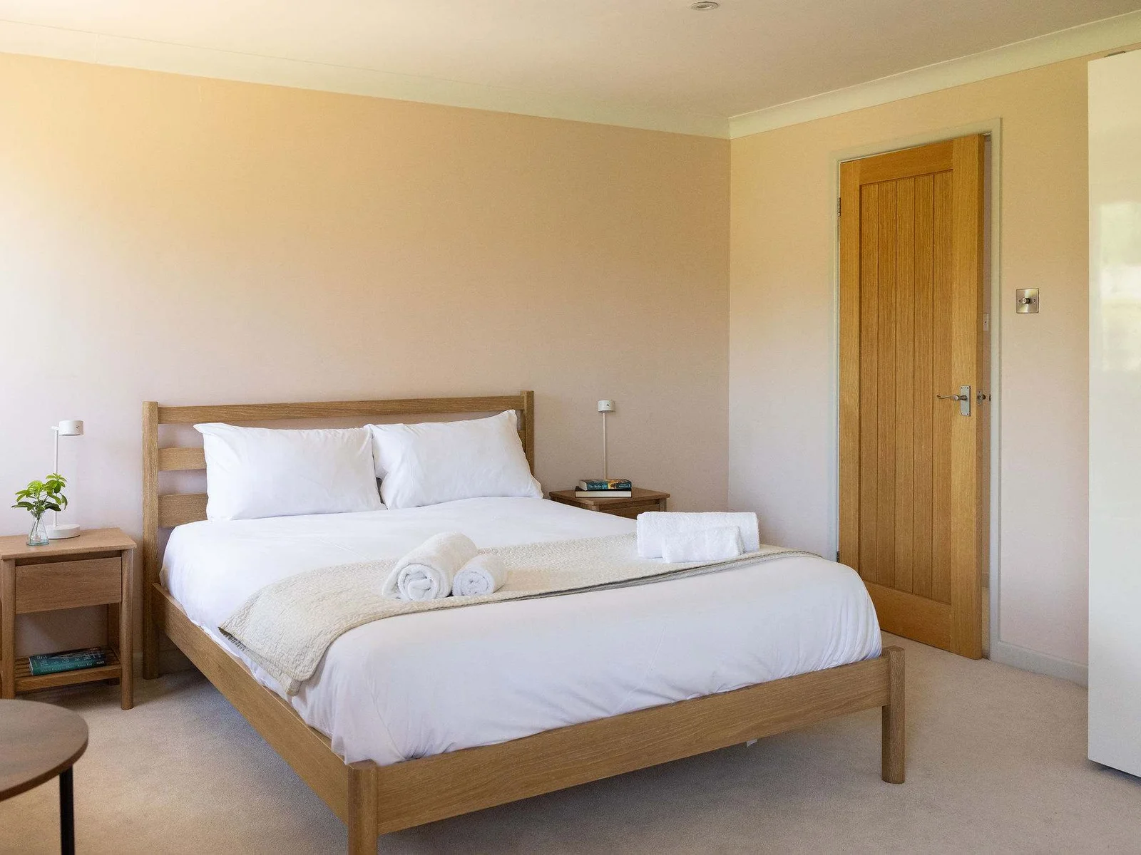 Spacious, light-filled master bedroom featuring a king-size bed, warm natural wood furniture, soft neutral tones, generous wardrobe storage, a dedicated dressing table, contemporary artwork and windows on two sides bringing in plenty of natural light