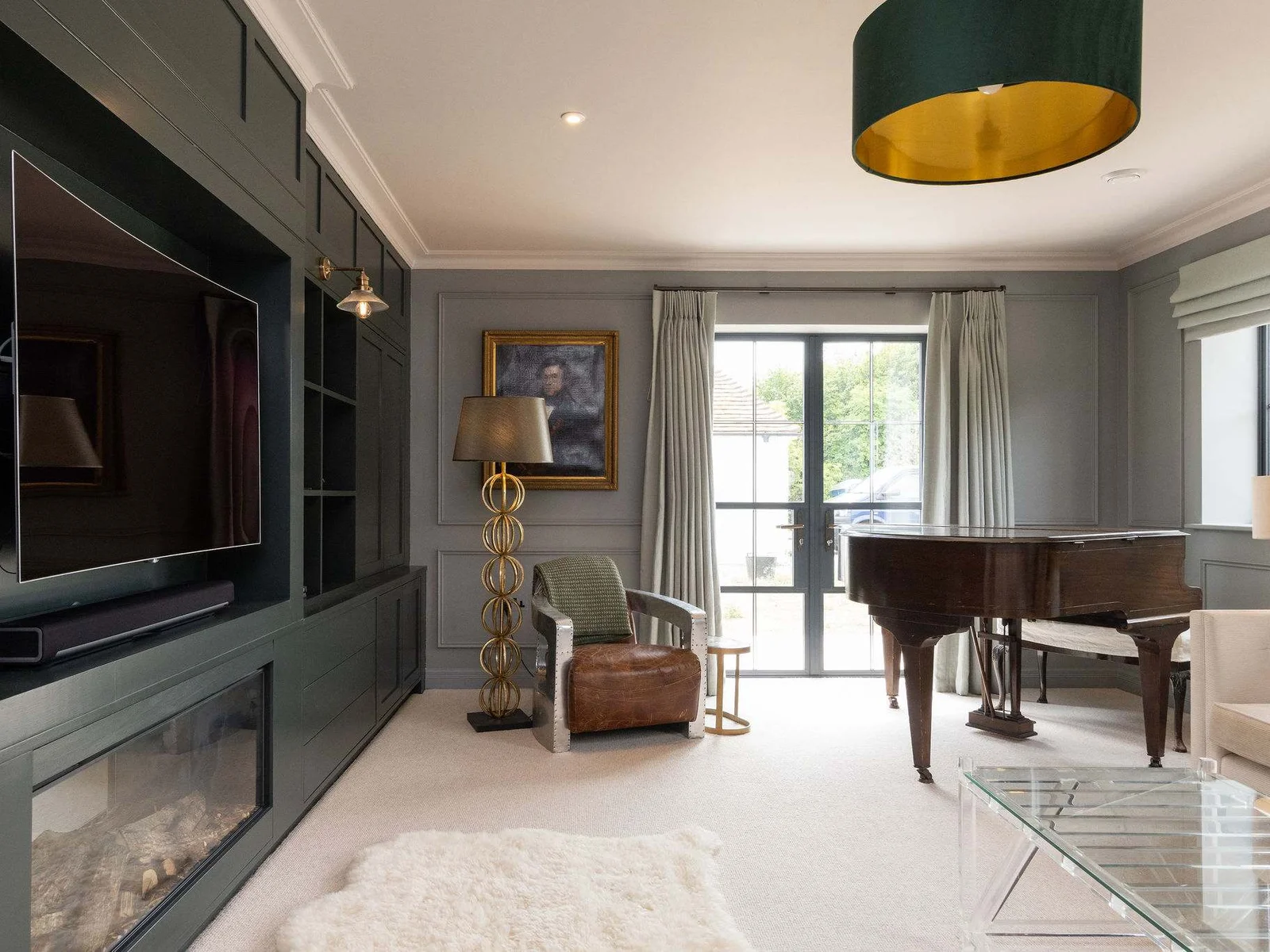 One of several elegant living spaces, featuring a grand piano, bespoke cabinetry, and garden views