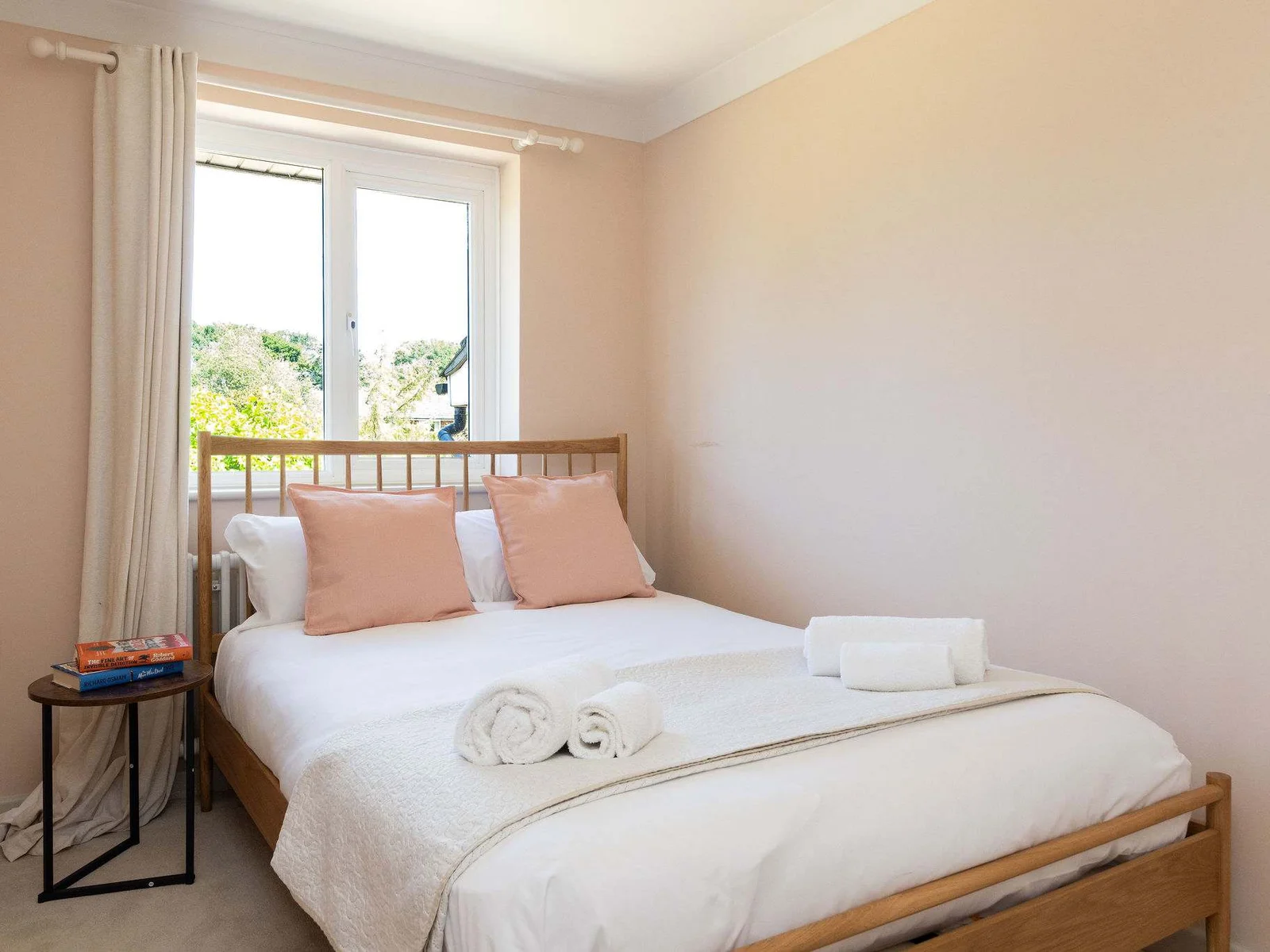 Soft blush tones, crisp white bedding and warm natural finishes give this double bedroom a calm, restful feel, with plenty of daylight coming through the window.