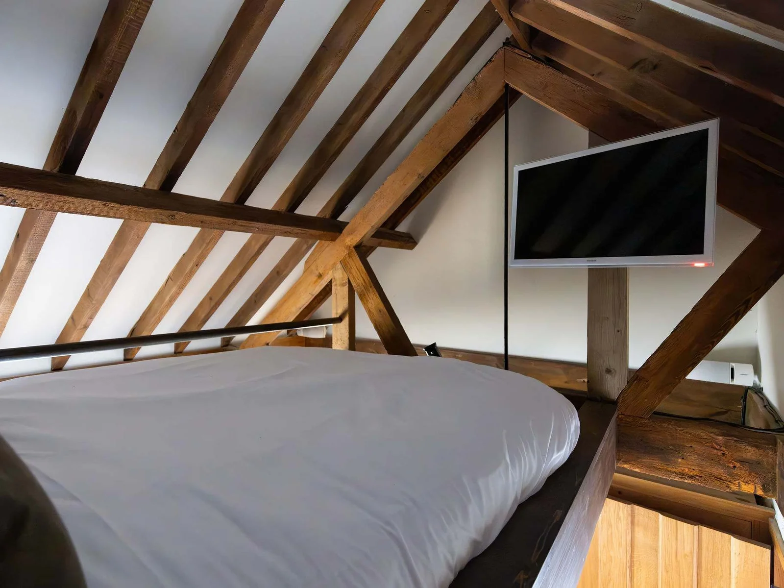A tucked-away mezzanine bedroom with exposed beams and its own TV
