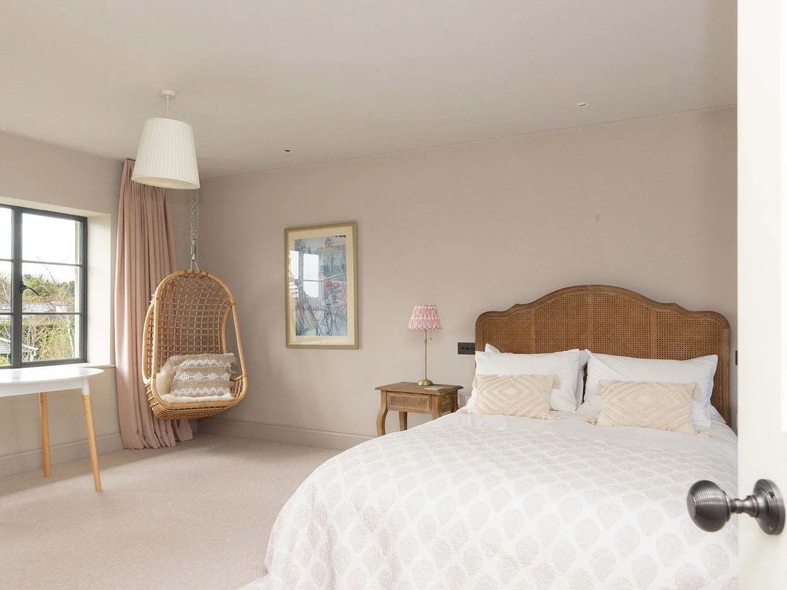 Charming double bedroom with a cosy hanging chair, soft tones, and garden views.
