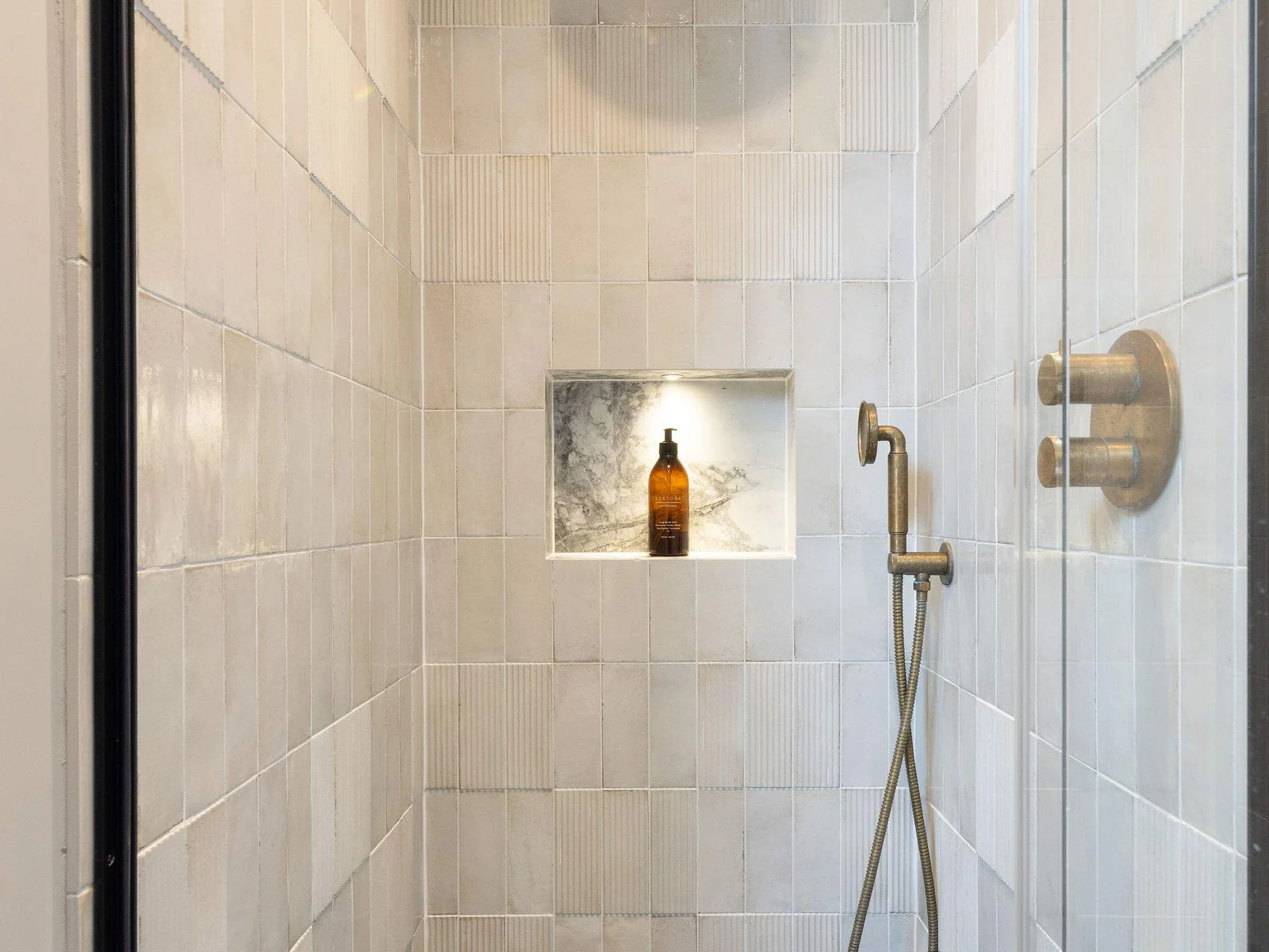 Stylish walk-in with brushed brass fixtures and a lit niche