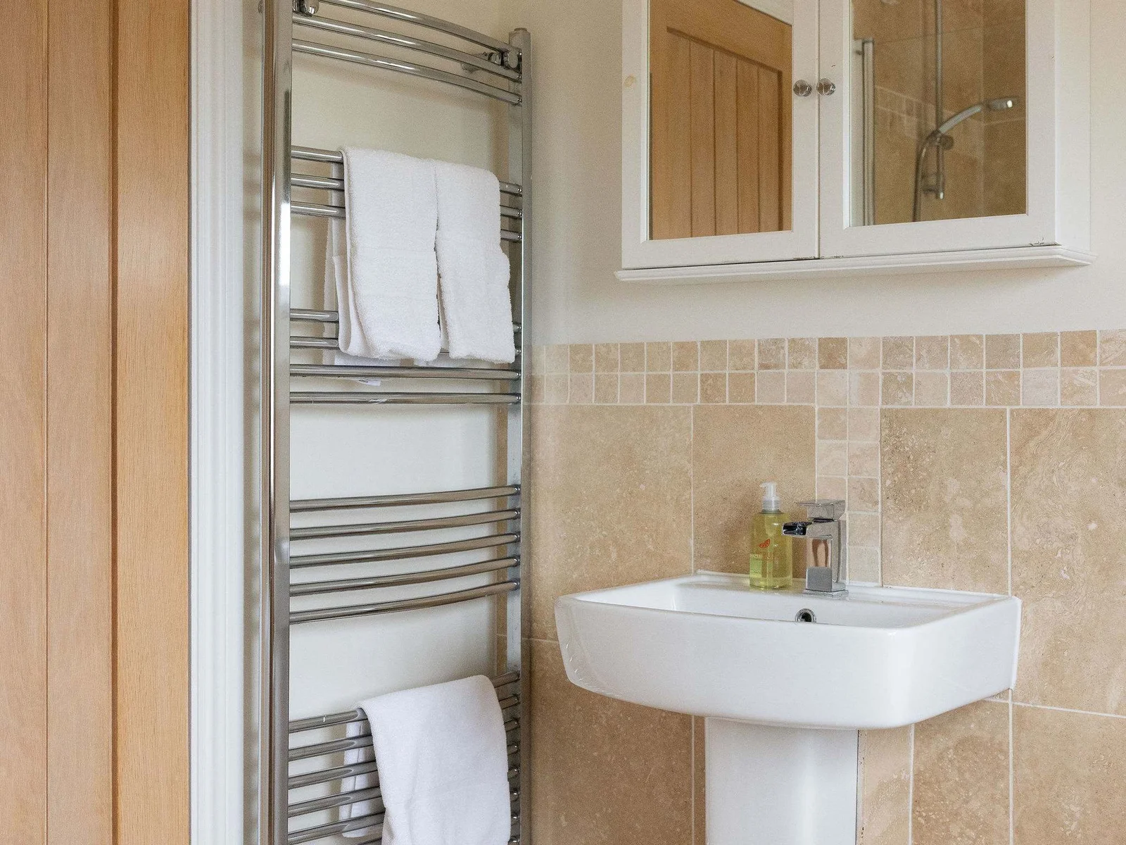 A polished corner of the family bathroom, with elegant stone finishes, a heated towel rail and mirrored storage.