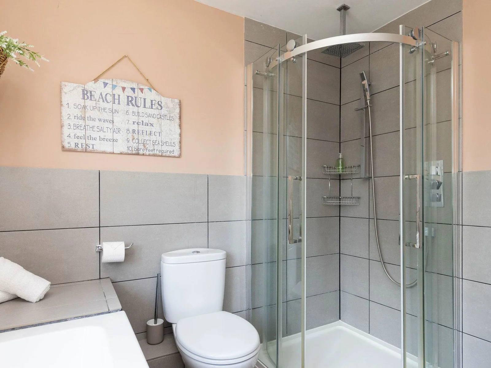 Soft blush walls and contemporary grey tiling give this shower room a fresh, stylish feel, with a glass-enclosed corner shower, WC, wide countertop and neatly arranged finishing touches.