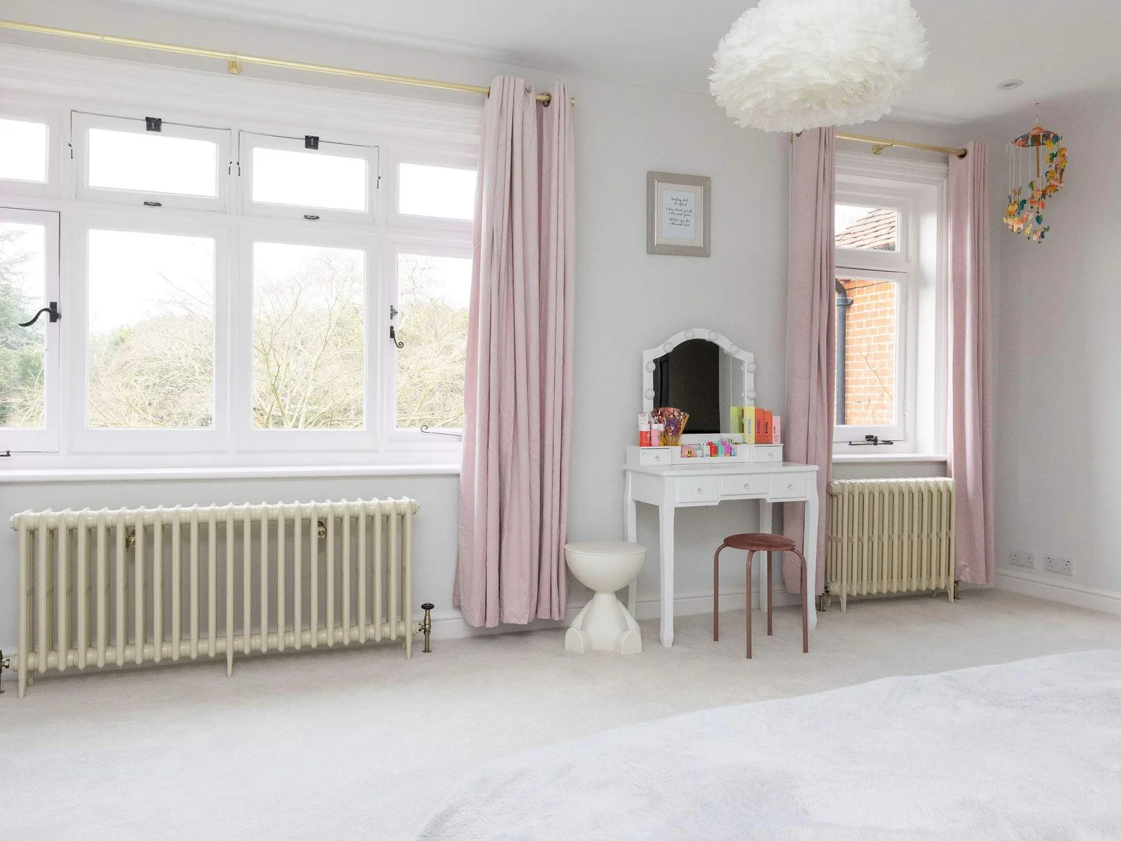 A spacious third bedroom with large windows, pink curtains, and a dressing table