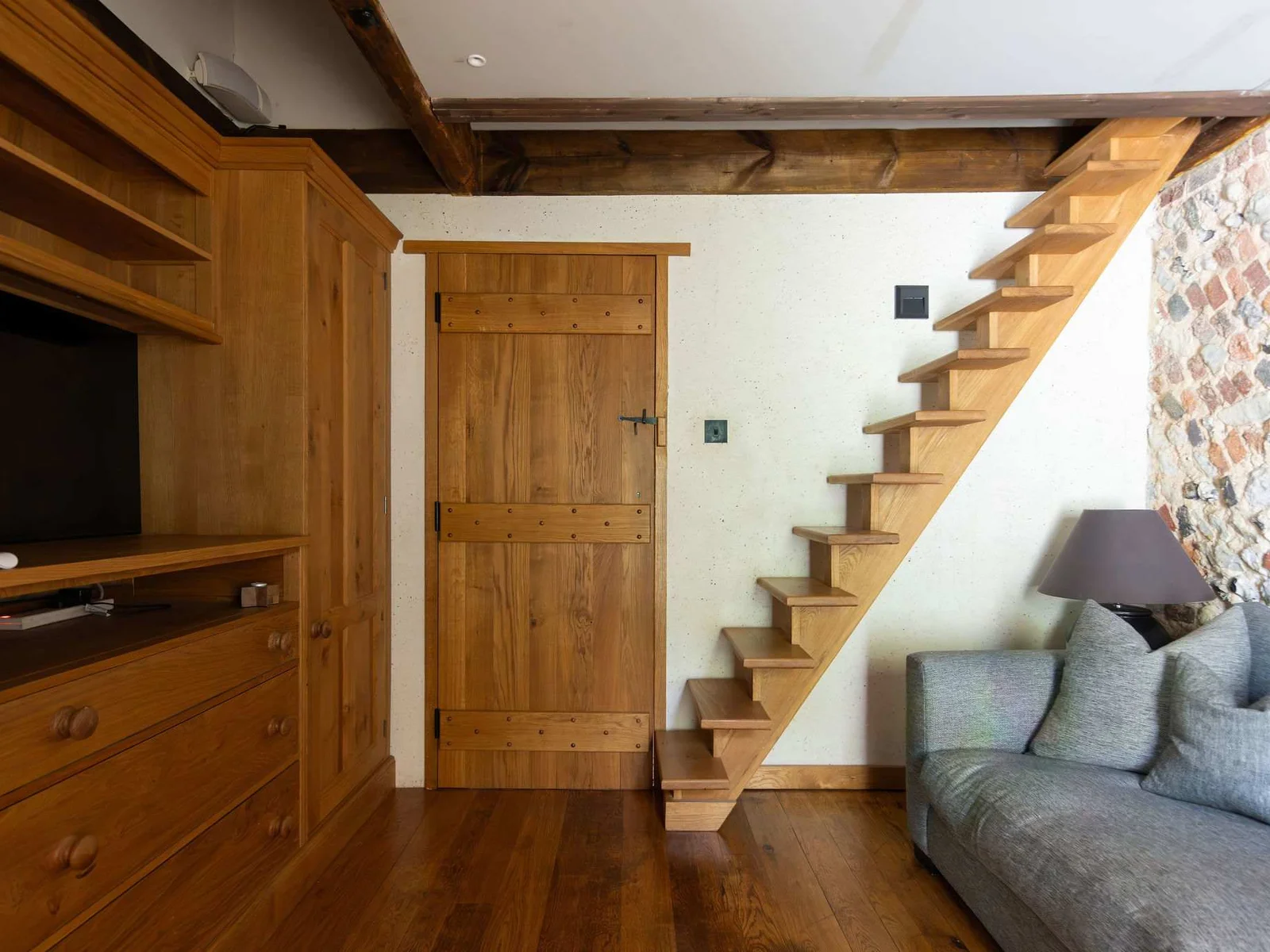 A cosy private lounge area with exposed flint, TV and stairs leading to the mezzanine bedroom.
