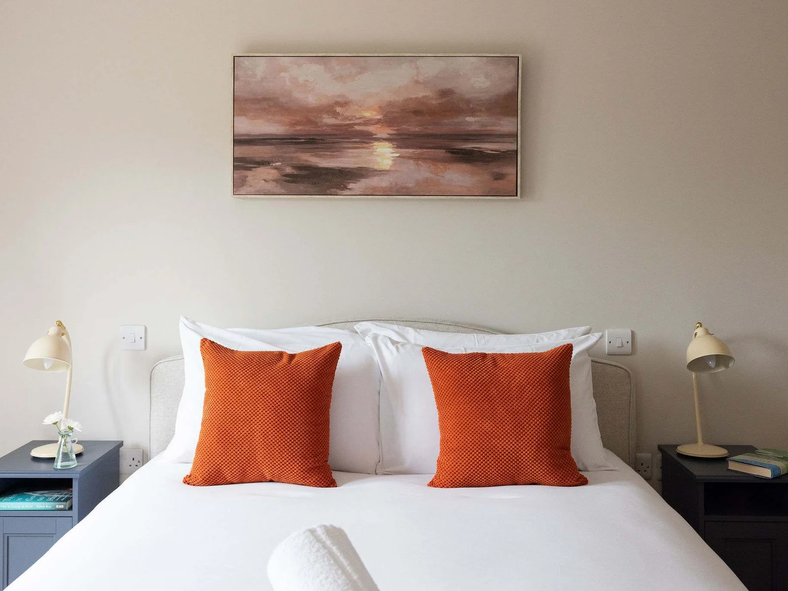The master bedroom, dressed with crisp white linen, warm burnt-orange accents and soft bedside lighting for a calm, cosy feel.