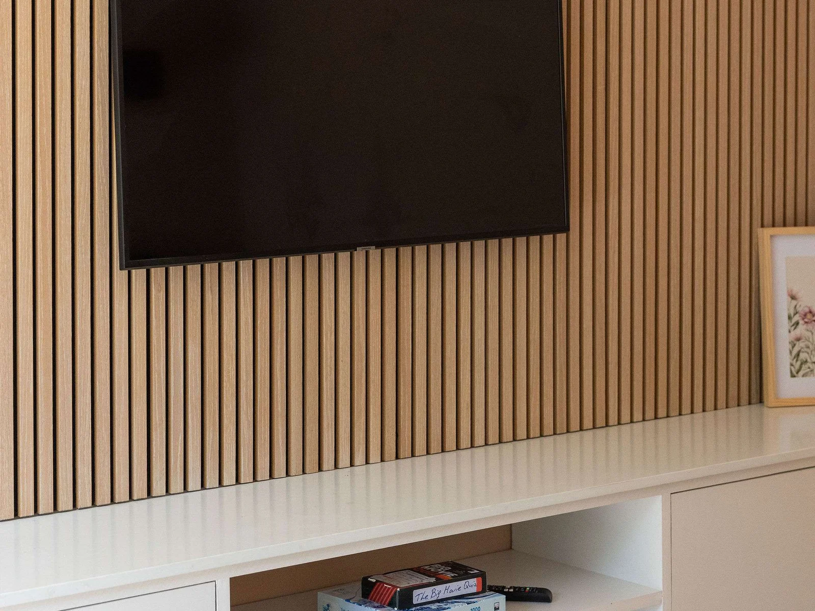 In the snug room a stylish media wall with warm timber slat detailing, a wall-mounted TV and sleek built-in storage, with a selection of games tucked below for relaxed nights in.