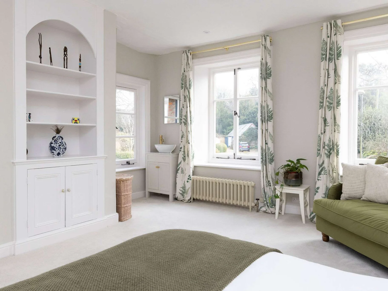 A light-filled bedroom with soft green accents and classic architectural details