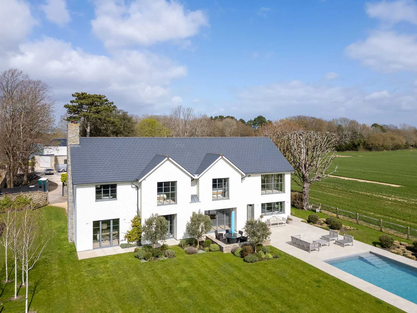 Aerial view showcasing the impressive home, heated pool, and surrounding open countryside setting.