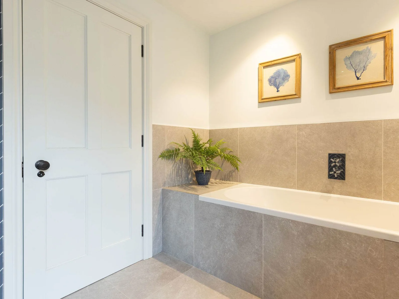 Relax in the elegant bathtub surrounded by natural stone tiles and charming coastal artwork.