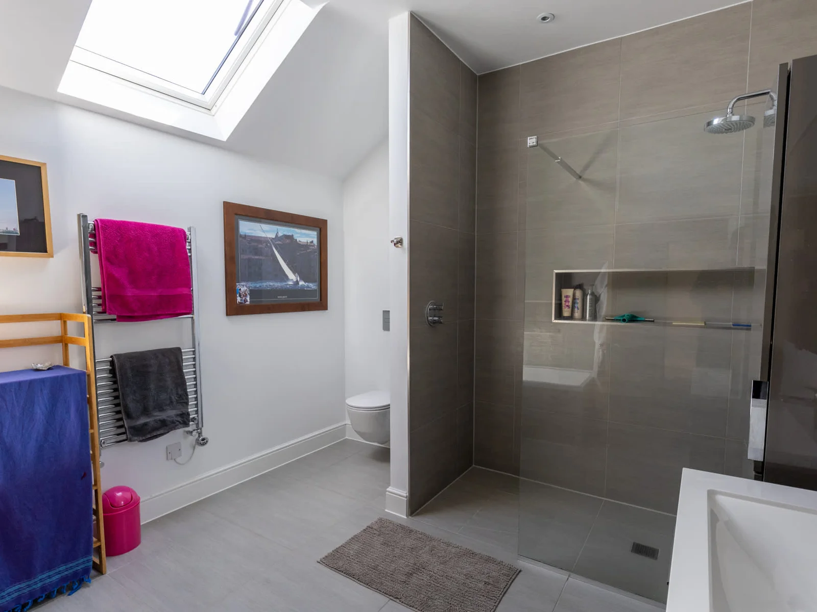 The bright, skylit bathroom serving the second floor — featuring a substantial walk-in shower with full-height grey tiles, and heated towel rail.