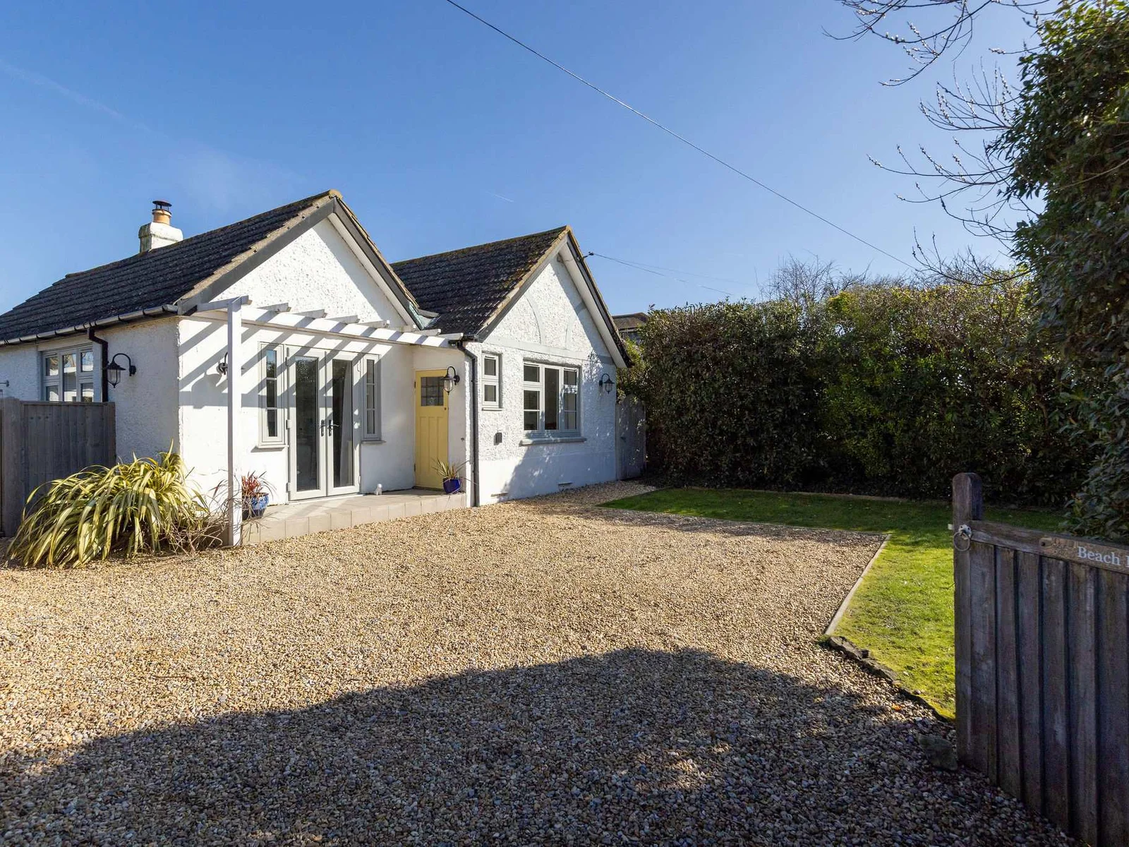 Beach Holme, showcases its inviting white exterior, pitched roofs, and a welcoming large gravel driveway to park multiple cars.