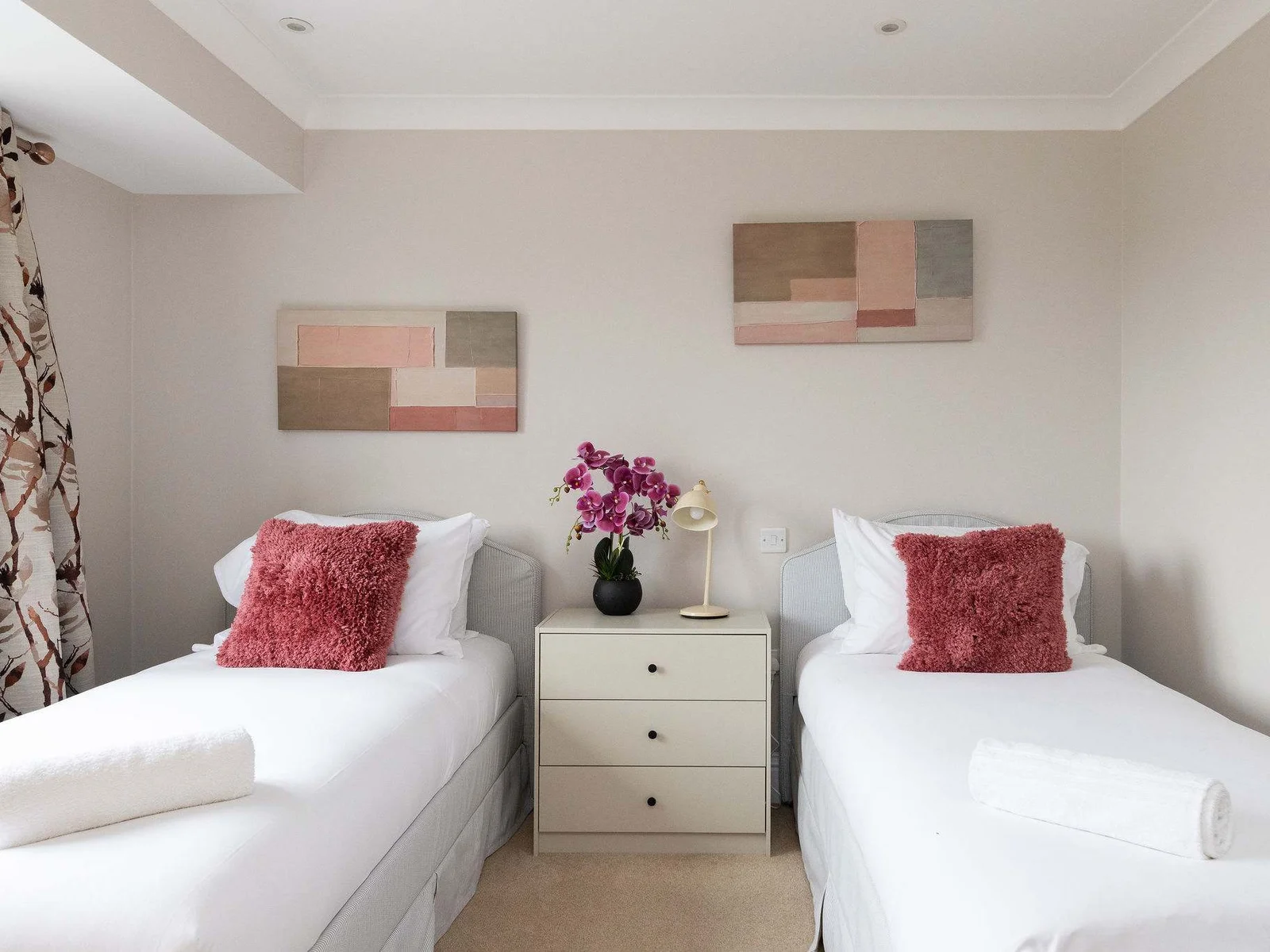 A stylish twin bedroom with crisp white linen, soft blush accents and elegant finishing touches — a lovely setup for children, friends or family sharing the room.