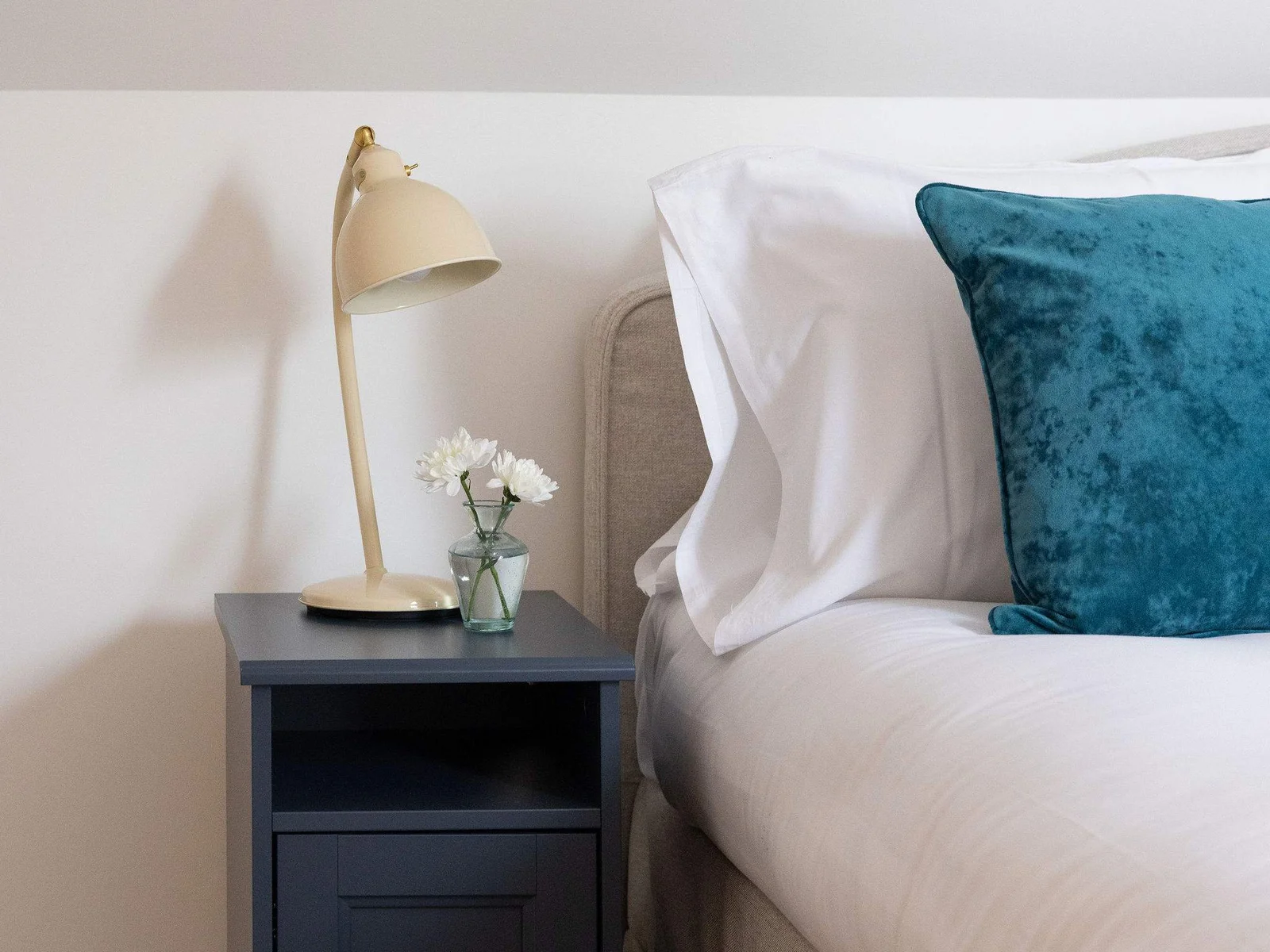 Soft bedside lighting, simple storage and subtle teal accents add a delicate finishing touch to this peaceful top-floor bedroom.