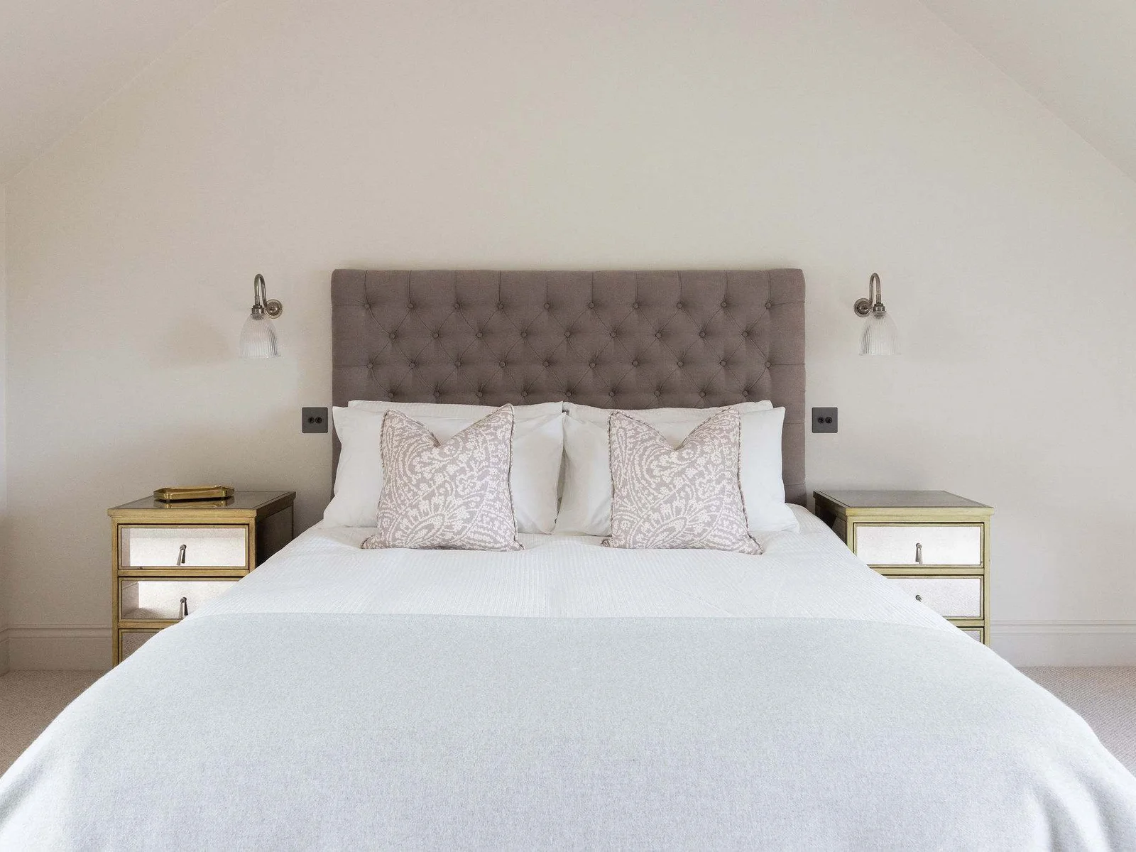 Luxurious king bedroom with tufted headboard, mirrored bedside tables, and crisp white linens.