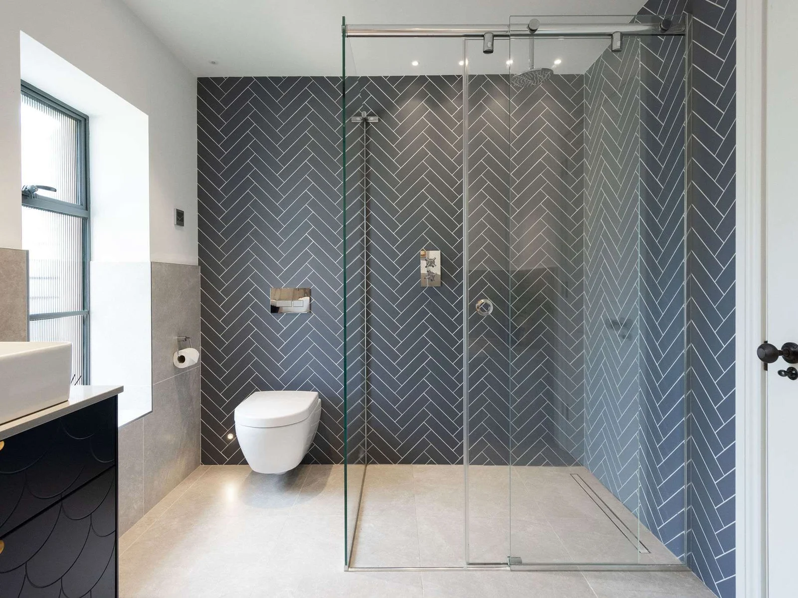 Striking herringbone-tiled walk-in shower with rainfall head, finished to the highest modern standard.