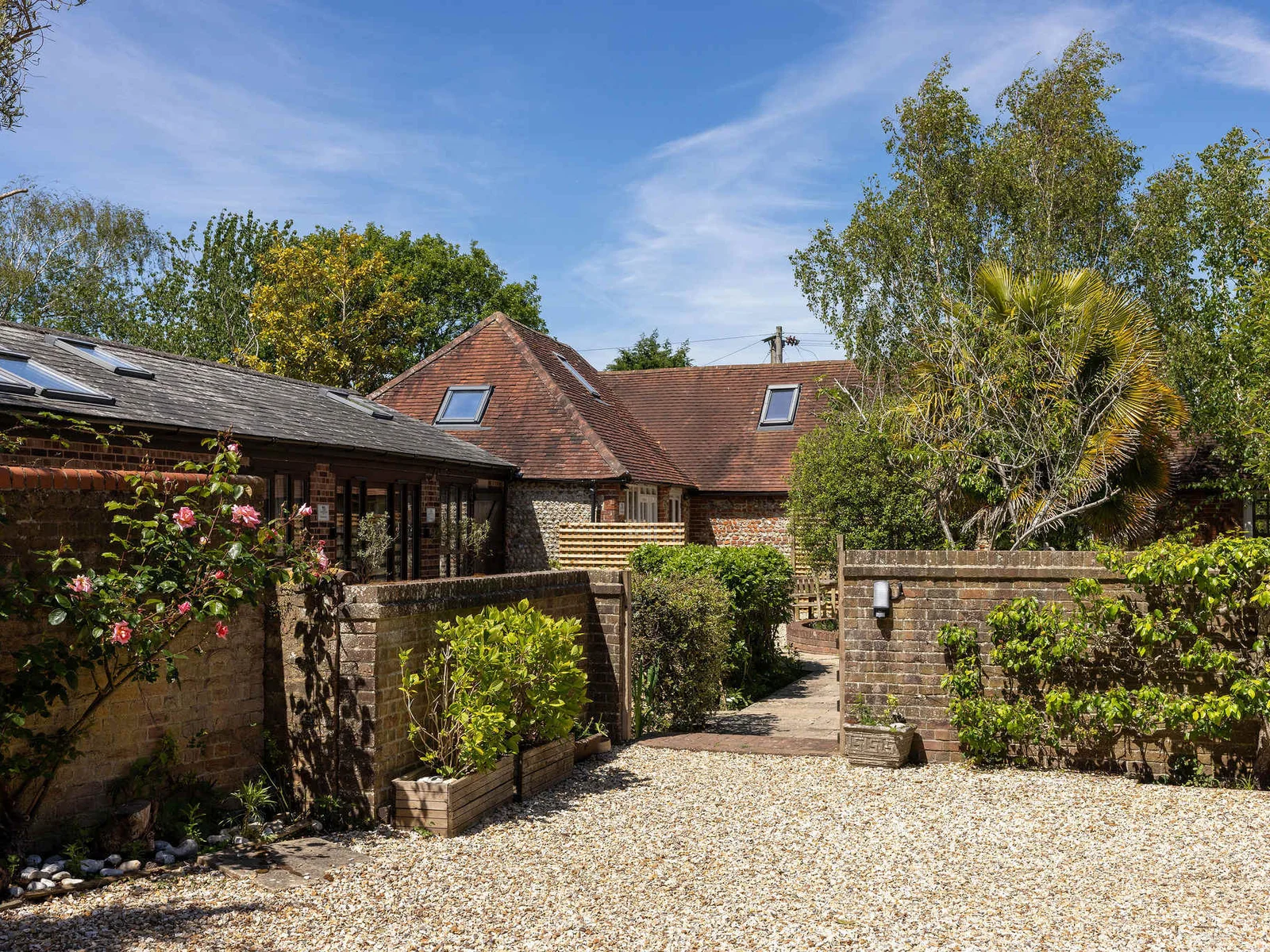 Pretty courtyard surroundings, with roses, trees and mature shrubs.
