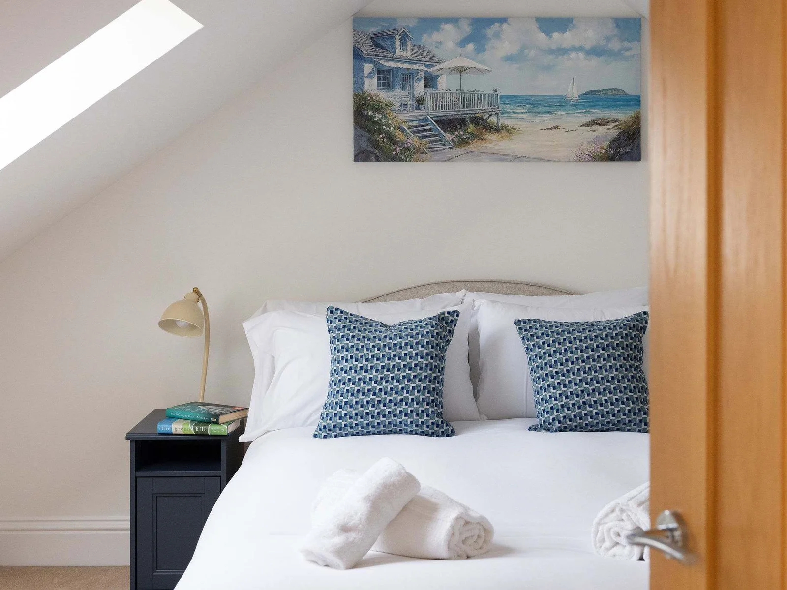 One of two bedrooms tucked away on the top floor, this cosy double has a lovely tucked-under-the-eaves feel with coastal artwork and thoughtful bedside touches.