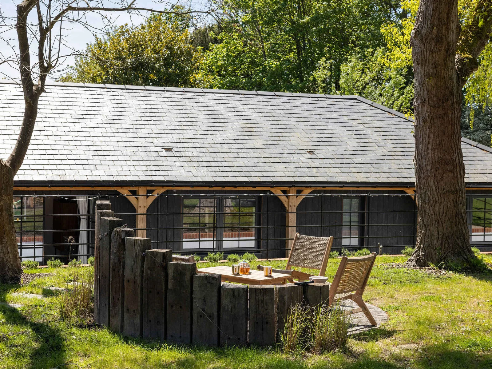 Sip morning tea beneath tall trees, with rustic seating tucked beside a tranquil countryside lodge.
