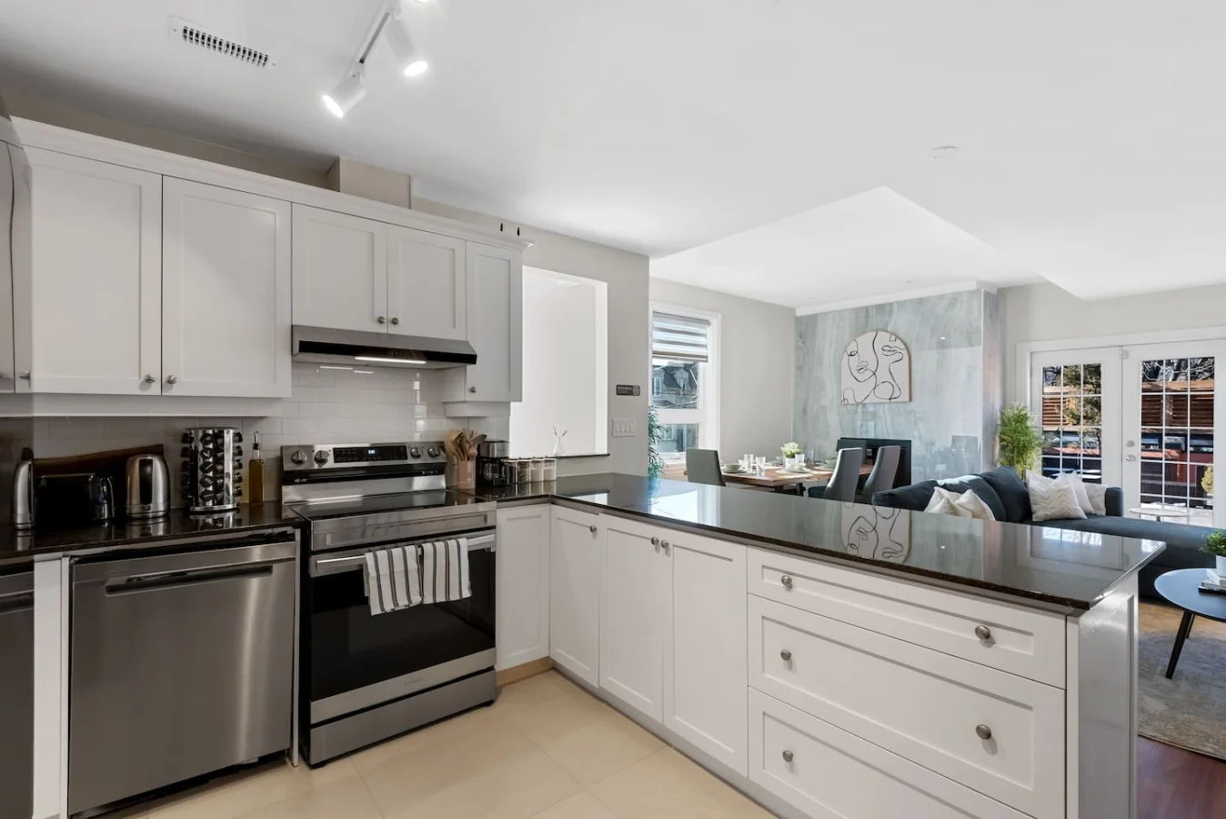 This modern kitchen features a spacious island with cabinetry, sleek white countertops, stainless steel appliances, open shelving, and stylish lighting.