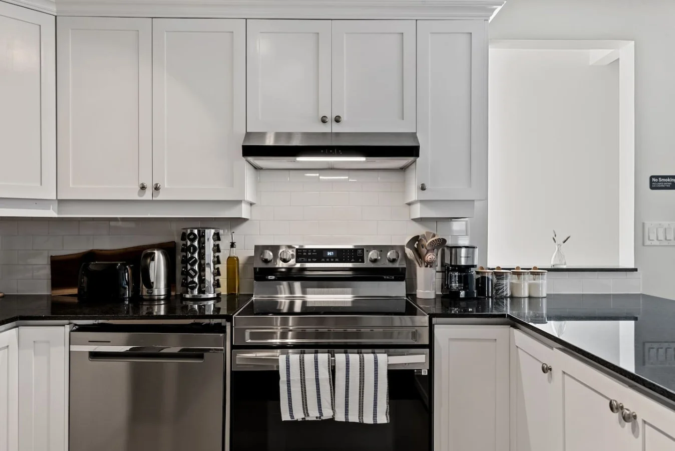 This modern kitchen features a spacious island with cabinetry, sleek white countertops, stainless steel appliances, open shelving, and stylish lighting.