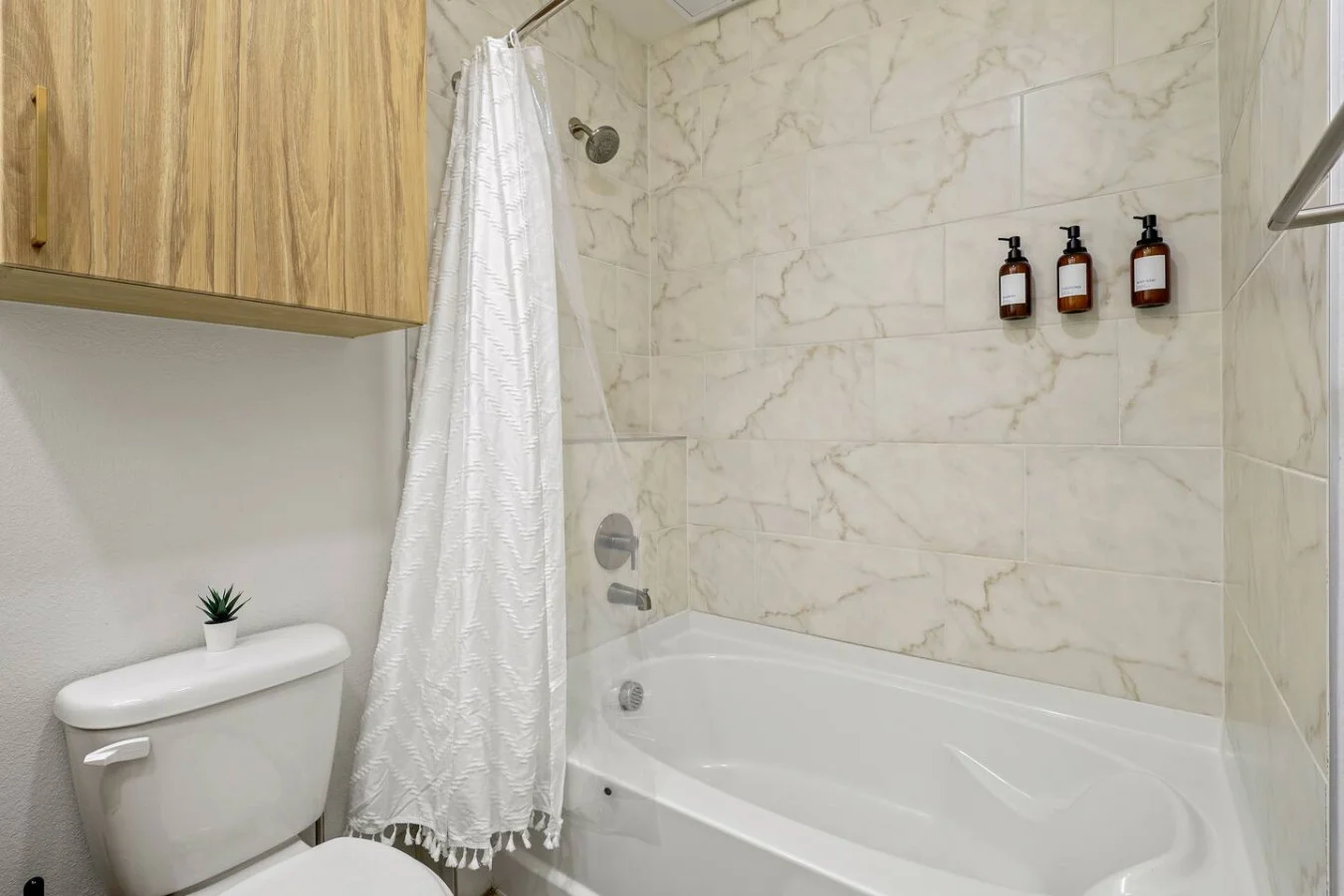 This bright and welcoming bathroom invites you to freshen up in comfort. Enjoy the forest-inspired shower curtain that adds a calming touch to your routine, complemented by the cozy rug underfoot and sparkling clean fixtures.