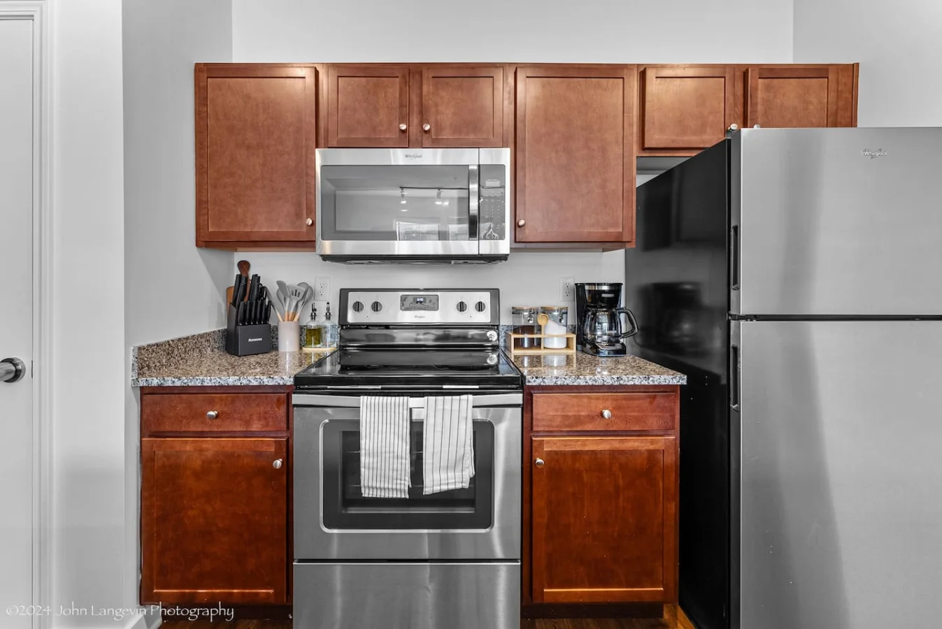 This modern kitchen features a spacious island with cabinetry, sleek white countertops, stainless steel appliances, open shelving, and stylish lighting.