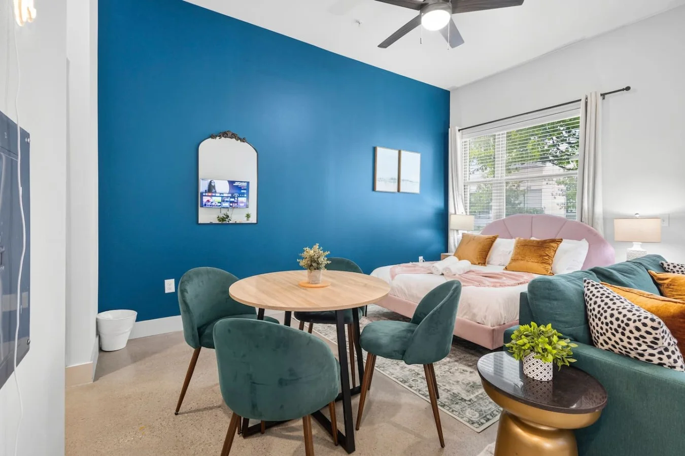 Charming dining corner featuring velvet green chairs and a round wooden table against a striking blue wall.