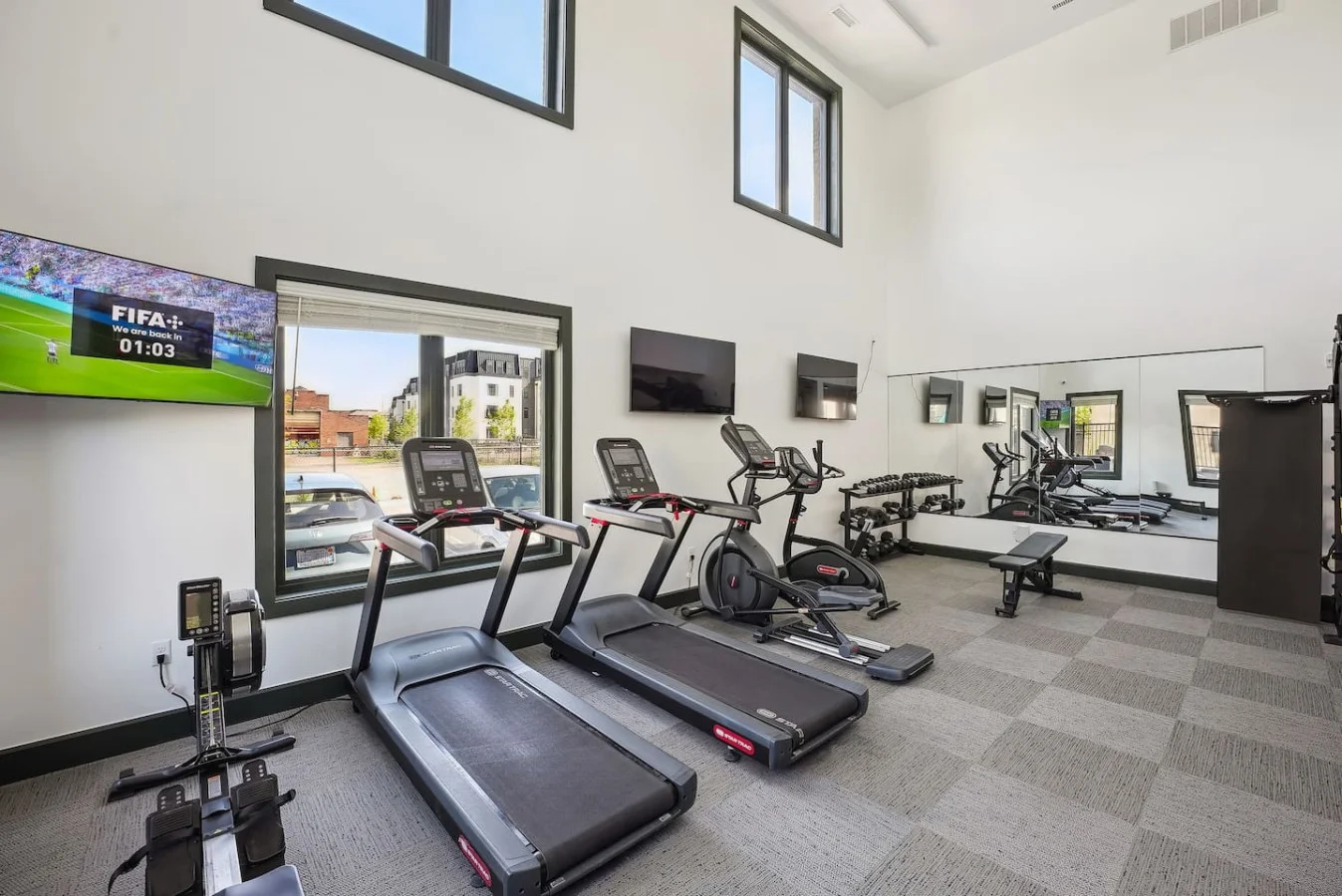 Spacious, well-lit gym equipped with a variety of cardio machines, free weights, and strength-training equipment.