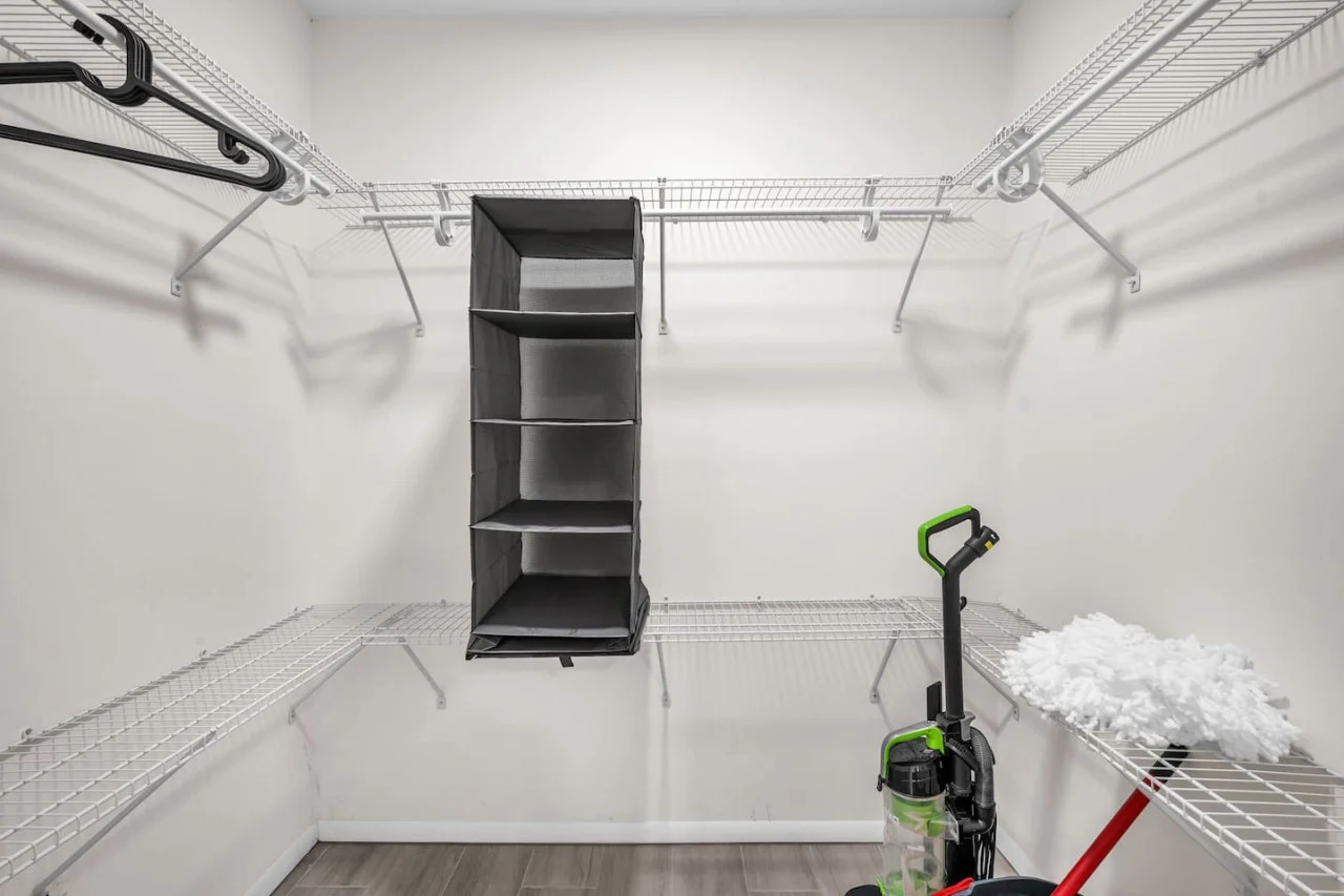 Spacious walk-in closet equipped with shelving, ample storage space, and cleaning essentials for guest use.