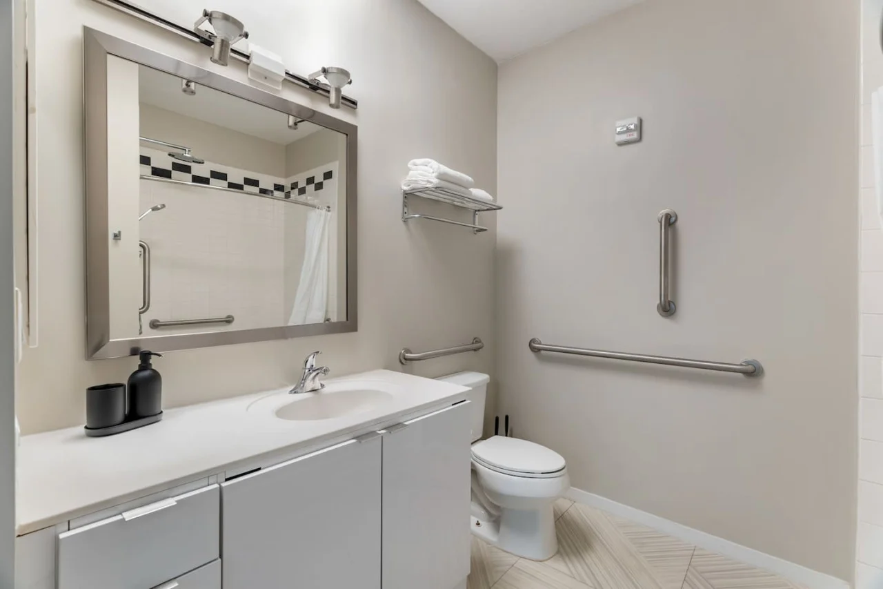 This bright and welcoming bathroom invites you to freshen up in comfort. Enjoy the forest-inspired shower curtain that adds a calming touch to your routine, complemented by the cozy rug underfoot and sparkling clean fixtures.