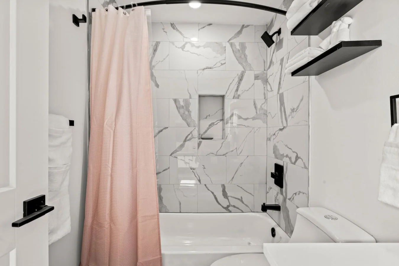 Modern bathroom with bath mat, toilet, shower area, and linens.