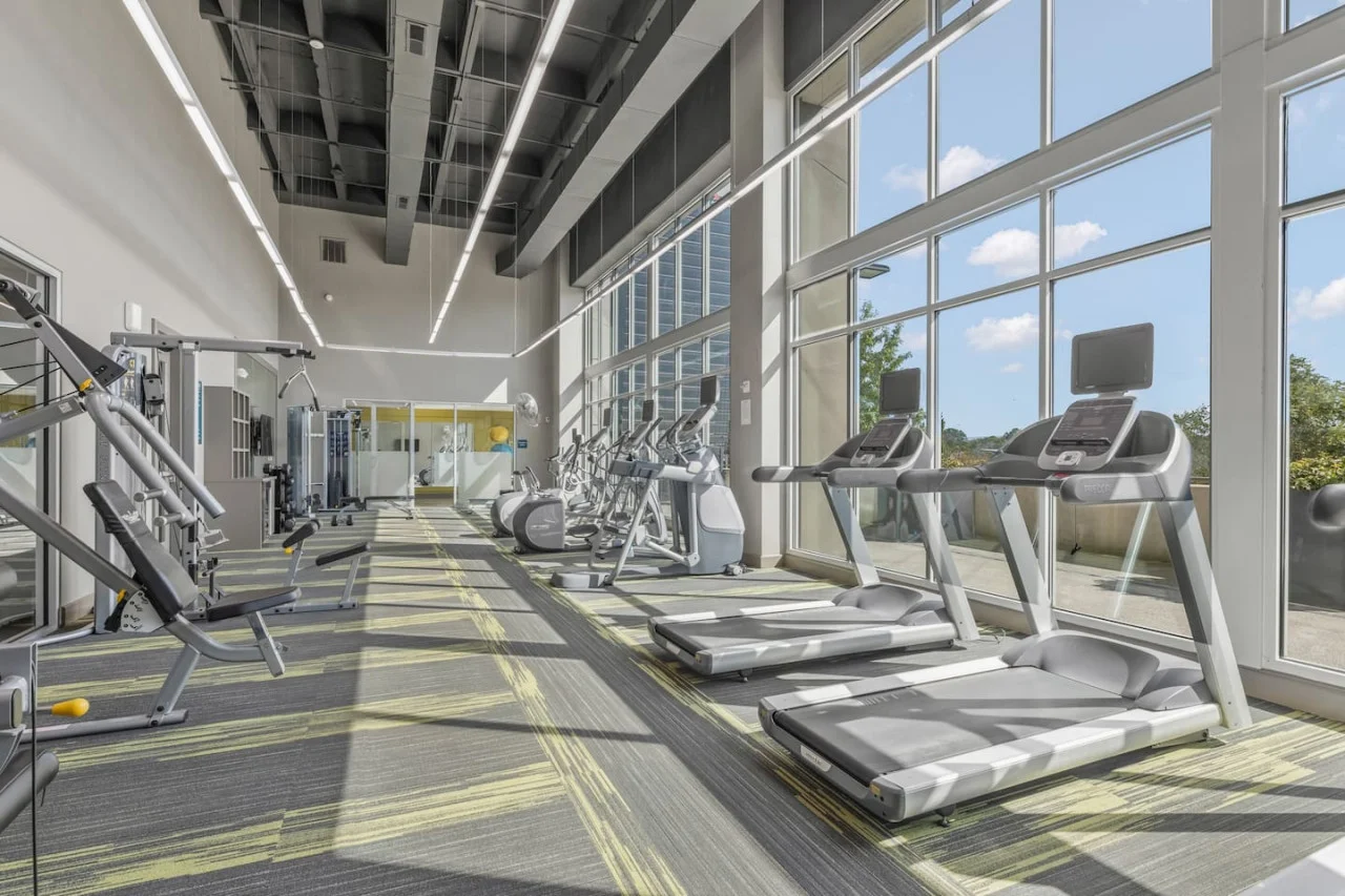 Spacious, well-lit gym equipped with a variety of cardio machines, free weights, and strength-training equipment.