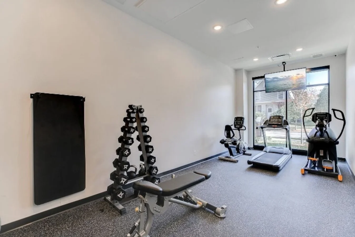 Spacious, well-lit gym equipped with a variety of cardio machines, free weights, and strength-training equipment.