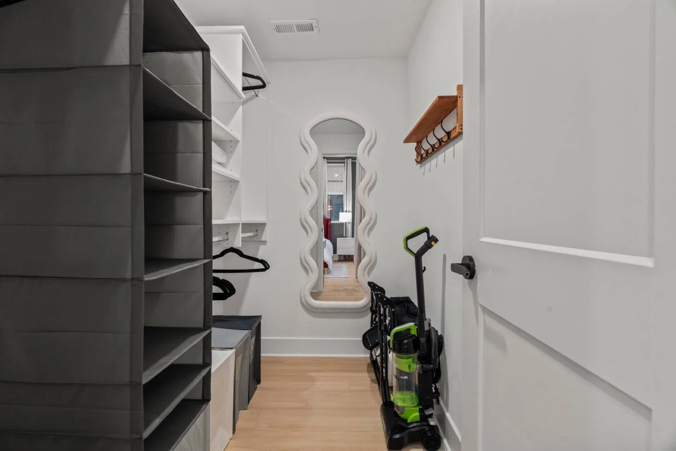 Closet area with full-length mirror, wagon, vacuum cleaner, hangers, and hooks.