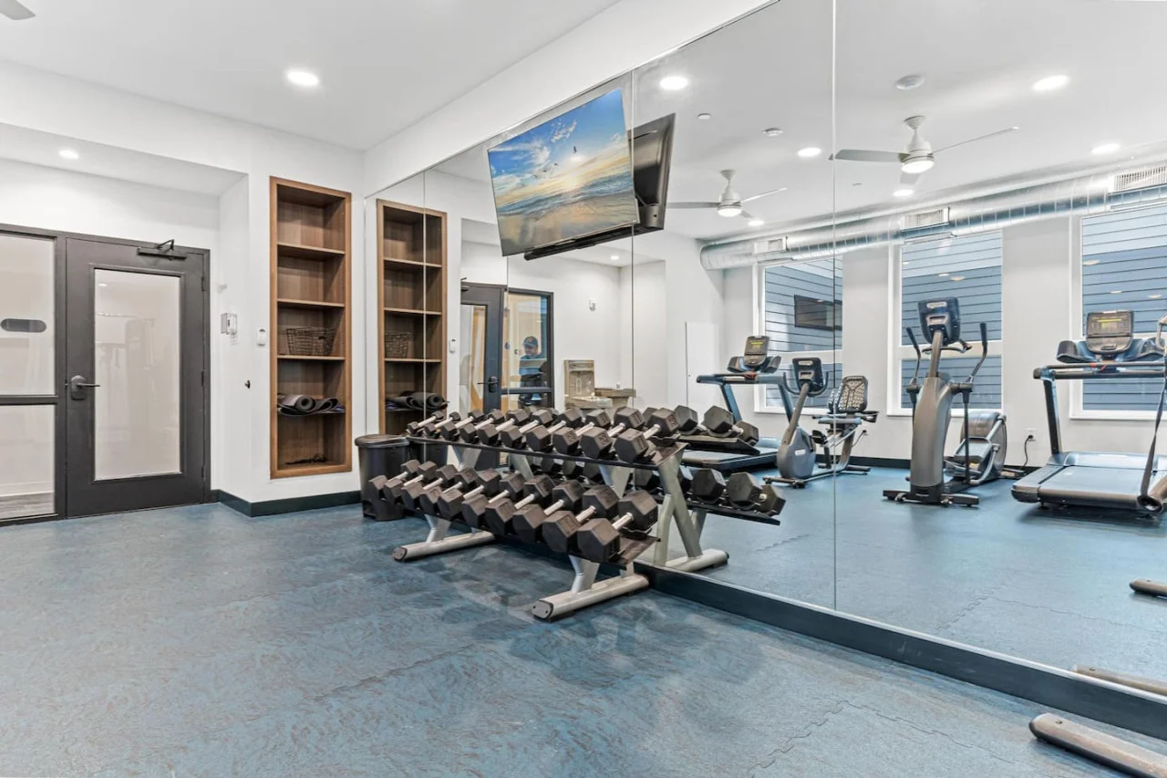 Spacious, well-lit gym equipped with a variety of cardio machines, free weights, and strength-training equipment.