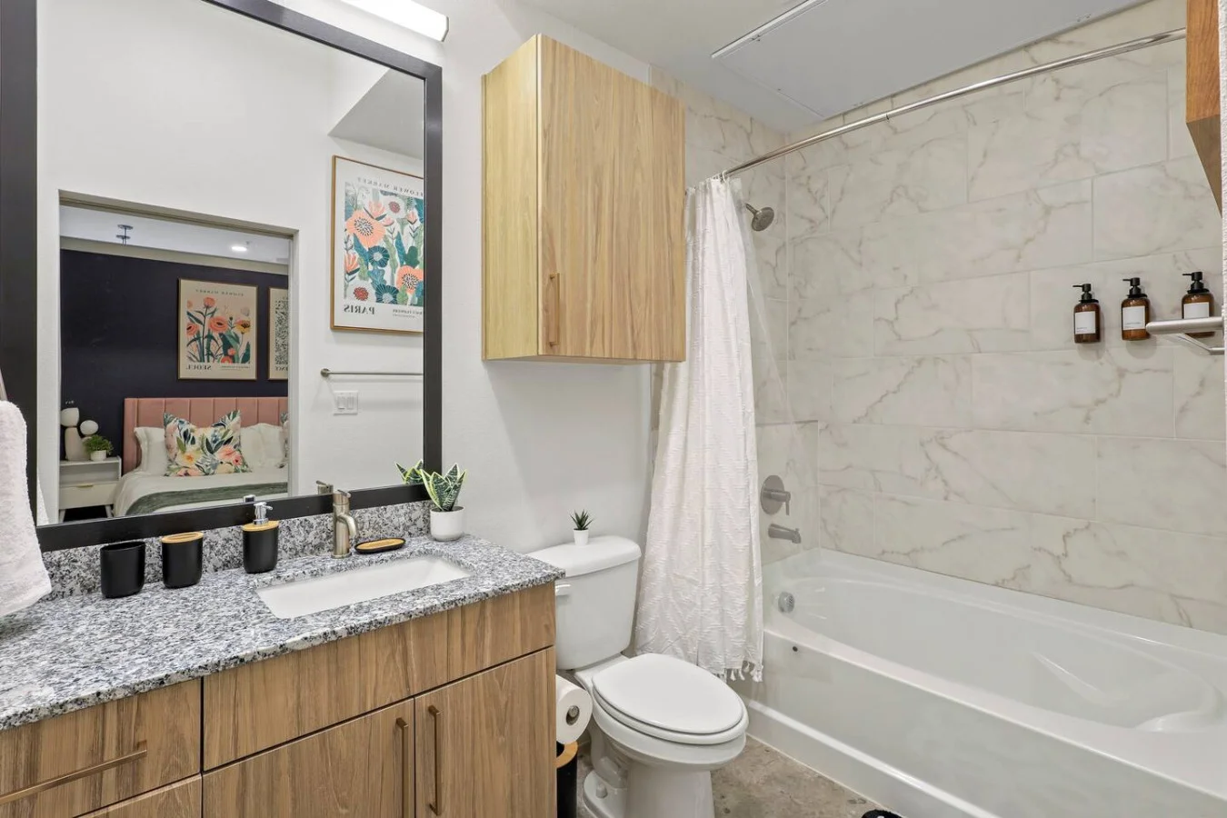 This bright and welcoming bathroom invites you to freshen up in comfort. Enjoy the forest-inspired shower curtain that adds a calming touch to your routine, complemented by the cozy rug underfoot and sparkling clean fixtures.