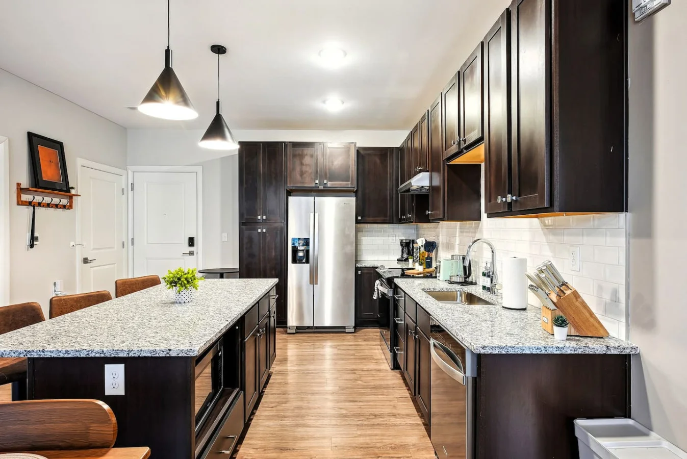 This modern kitchen features a spacious island with cabinetry, sleek white countertops, stainless steel appliances, open shelving, and stylish lighting.