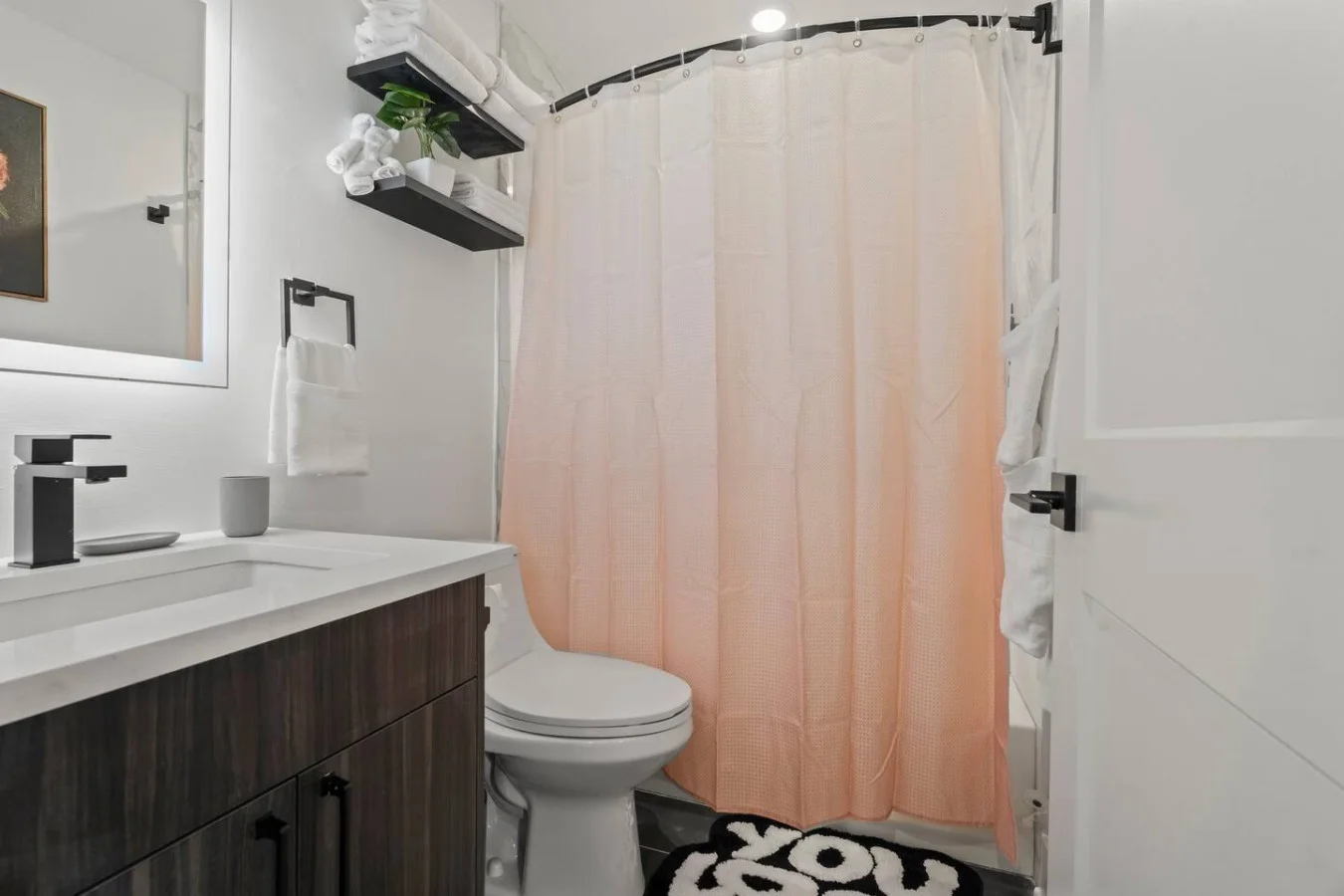 Modern bathroom with bath mat, toilet, shower area, and linens.