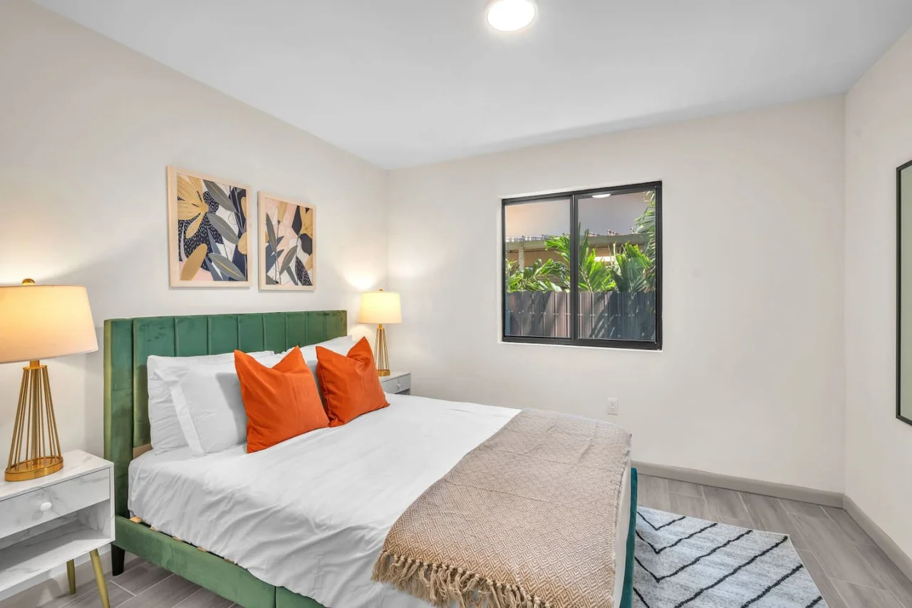 Bright and airy bedroom with simple yet modern decor, complemented by a large window for natural light and outdoor views.