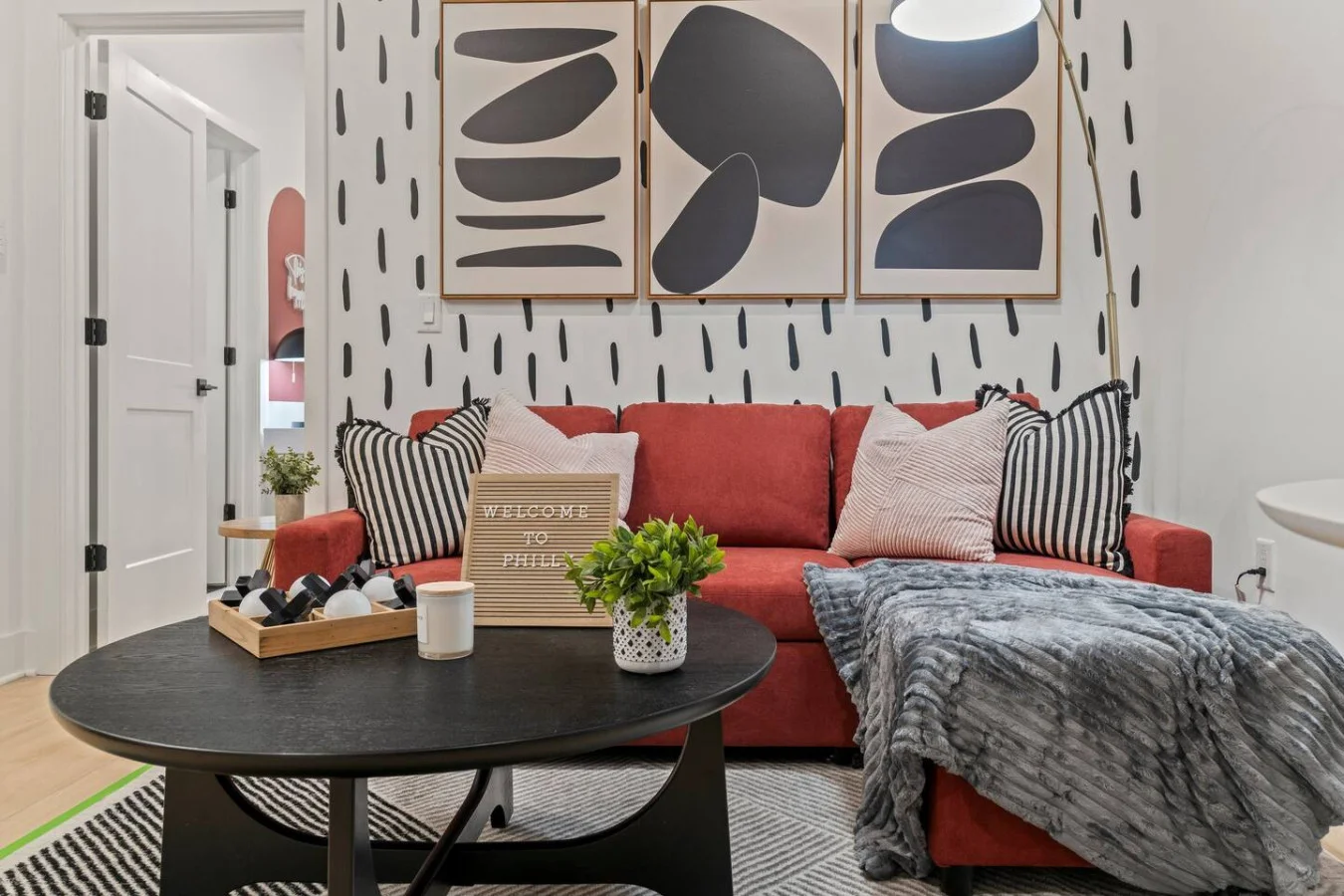 Chic living space with a bold red sofa, modern art, and cozy touches for a warm Philly welcome.