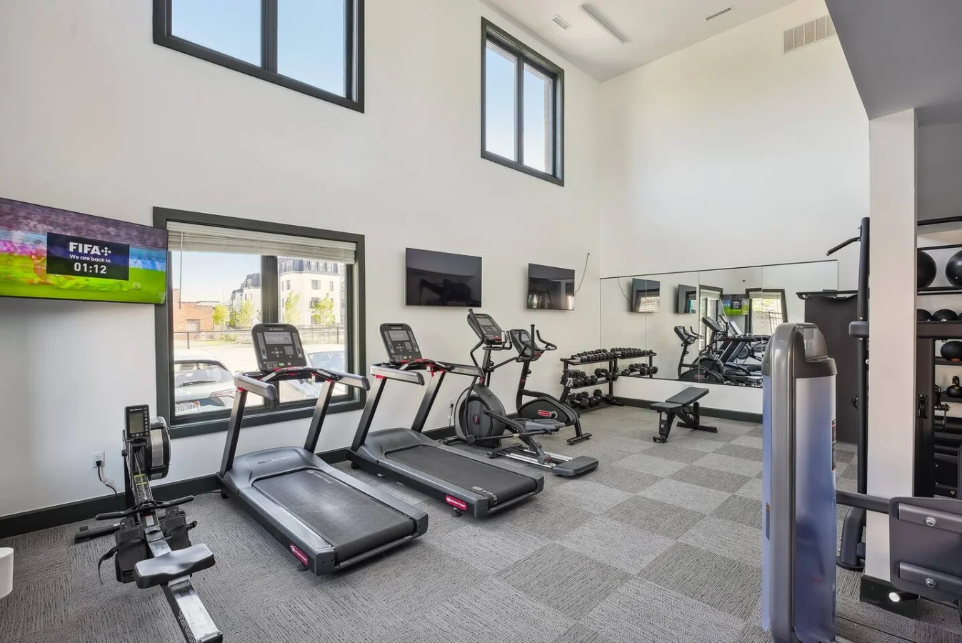Spacious, well-lit gym equipped with a variety of cardio machines, free weights, and strength-training equipment.