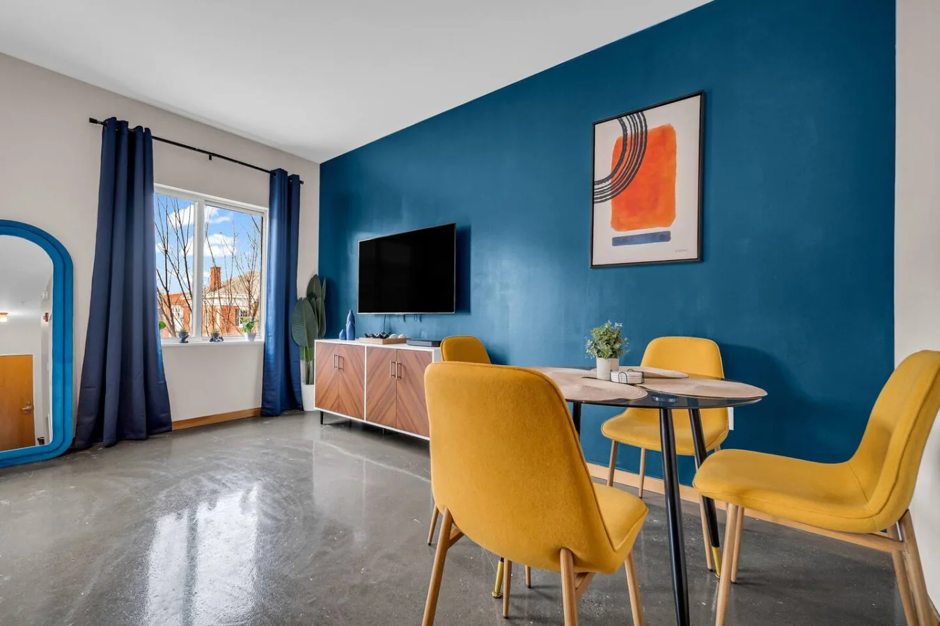 Spacious open-concept living and dining area featuring a vibrant blue sofa, modern furnishings, and a stylish entertainment setup—ideal for gatherings and relaxation.