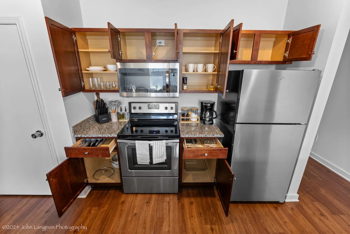 This modern kitchen features a spacious island with cabinetry, sleek white countertops, stainless steel appliances, open shelving, and stylish lighting.