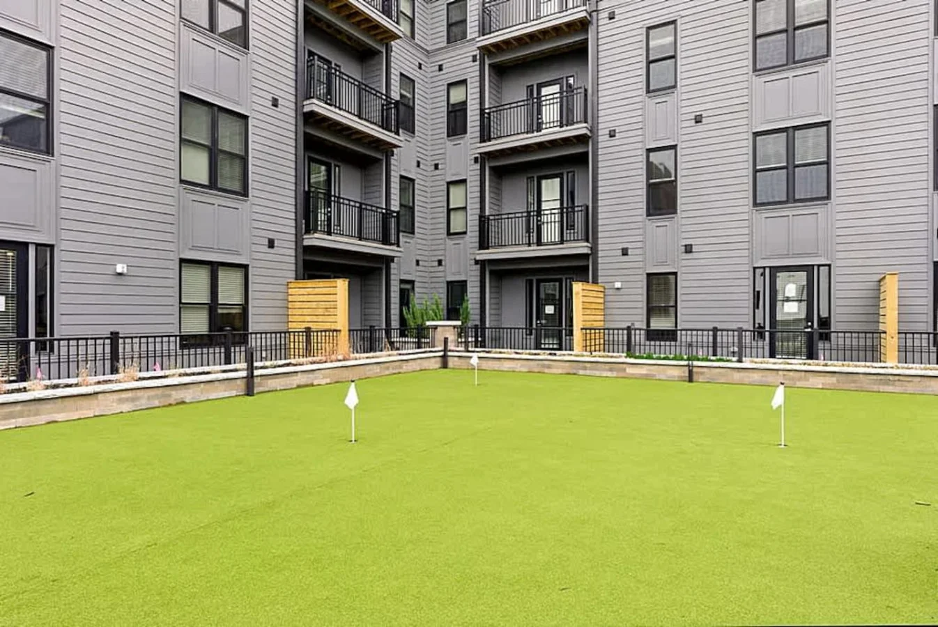 A beautiful green courtyard with manicured turf surrounded by modern apartment facades. This open space is perfect for relaxing outdoors, enjoying fresh air, or spending time in a peaceful community atmosphere.