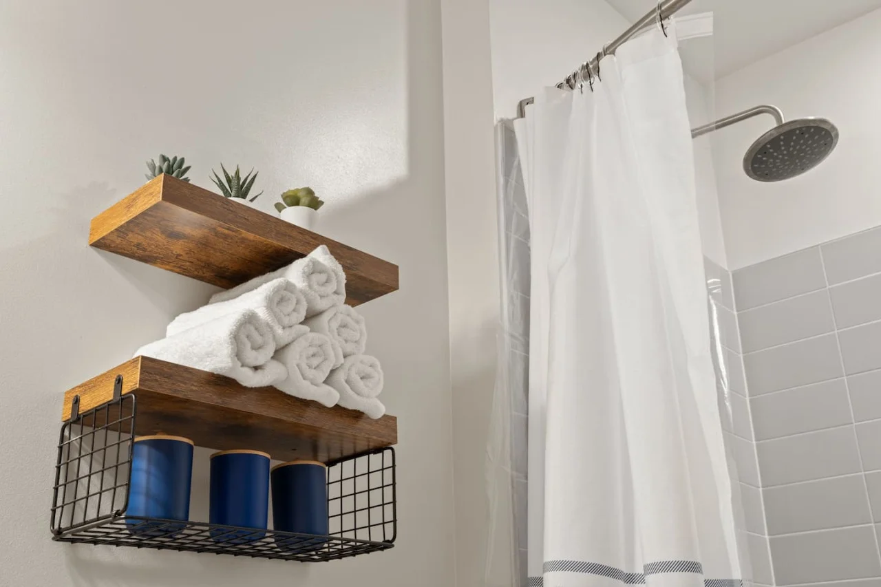This bright and welcoming bathroom invites you to freshen up in comfort. Enjoy the forest-inspired shower curtain that adds a calming touch to your routine, complemented by the cozy rug underfoot and sparkling clean fixtures.