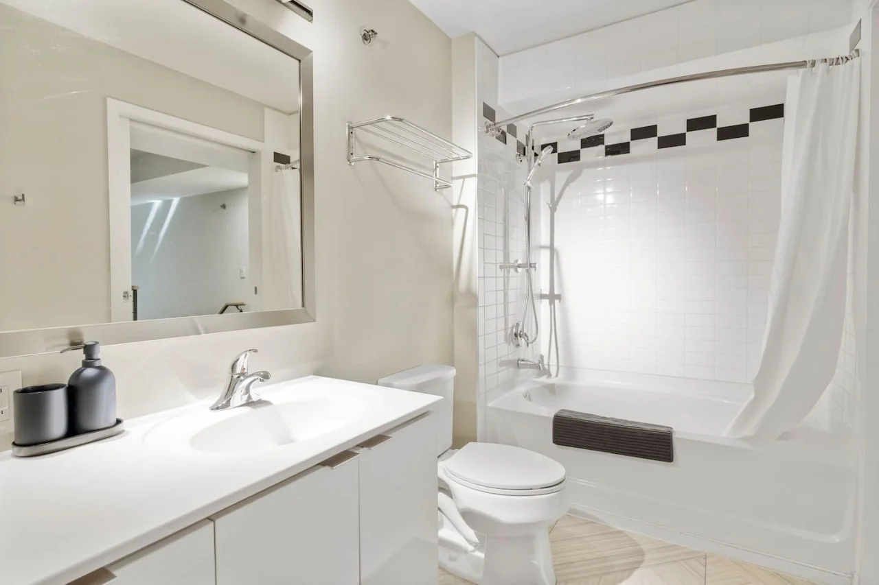 This bright and welcoming bathroom invites you to freshen up in comfort. Enjoy the forest-inspired shower curtain that adds a calming touch to your routine, complemented by the cozy rug underfoot and sparkling clean fixtures.