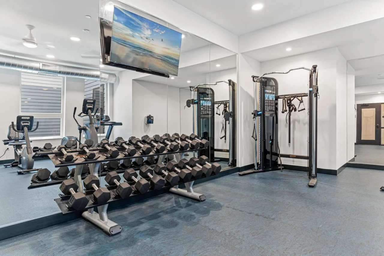 Spacious, well-lit gym equipped with a variety of cardio machines, free weights, and strength-training equipment.