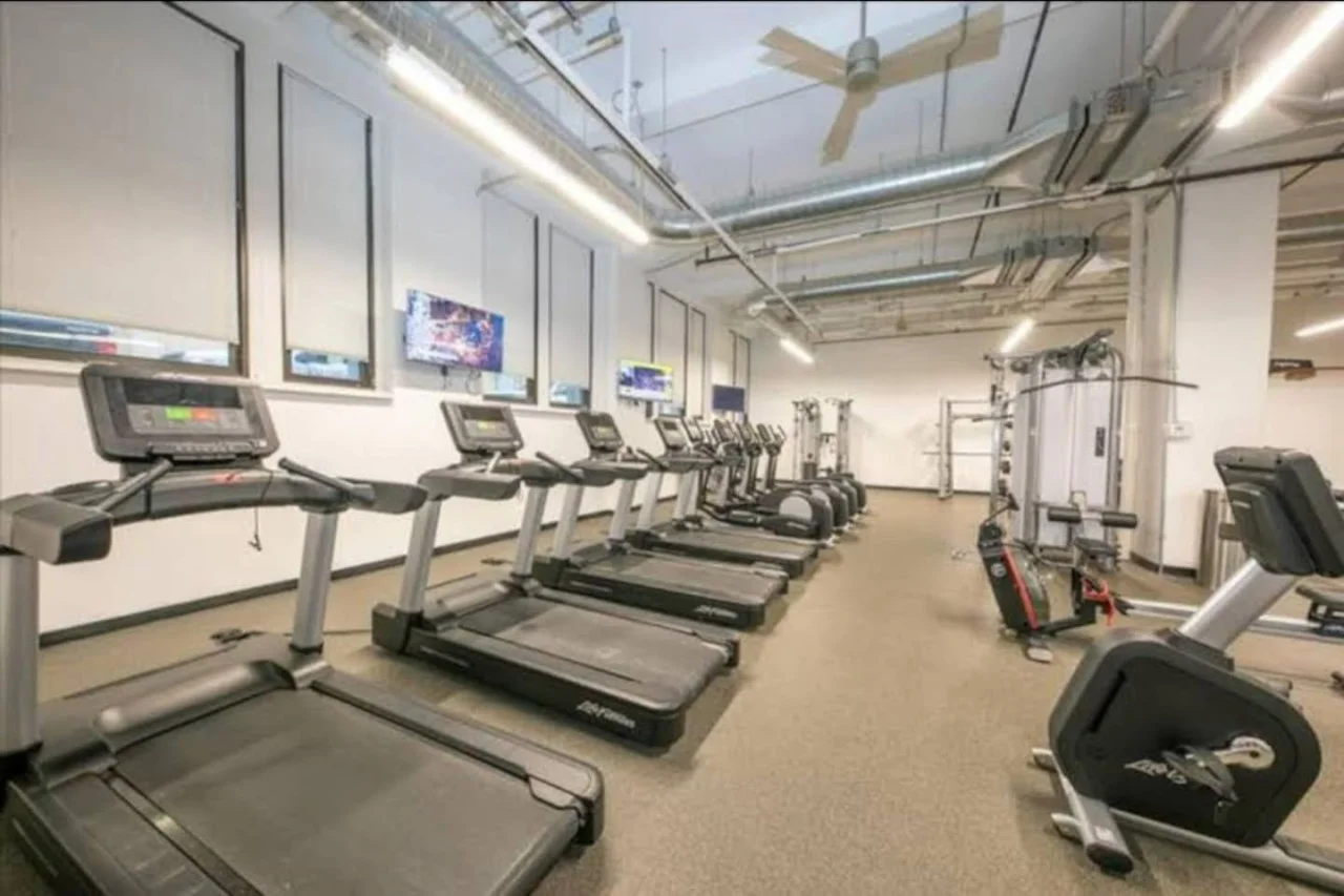 Spacious, well-lit gym equipped with a variety of cardio machines, free weights, and strength-training equipment.